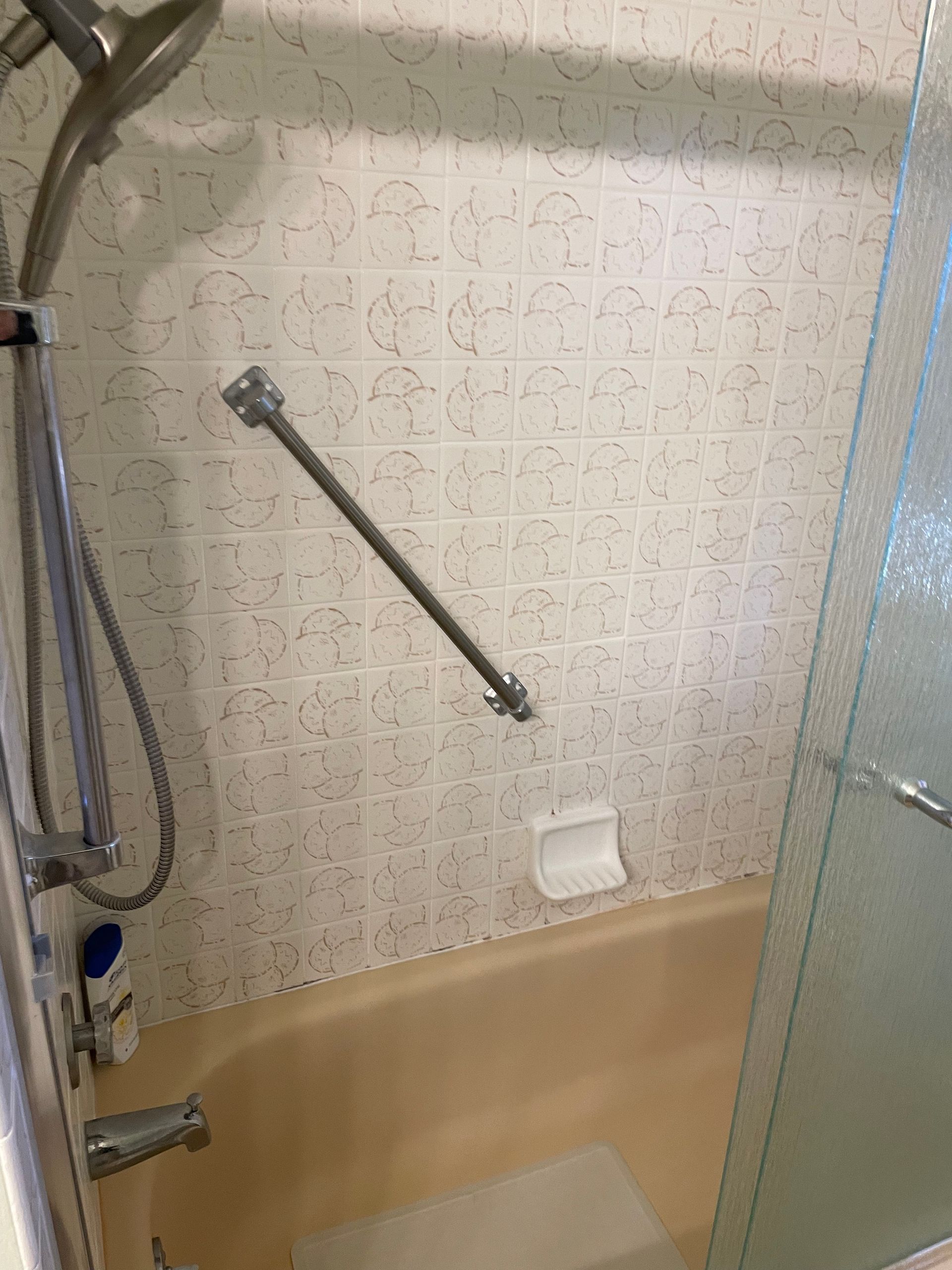 Bathtub shower area with beige tile, glass partition, grab bars, and a handheld shower hose