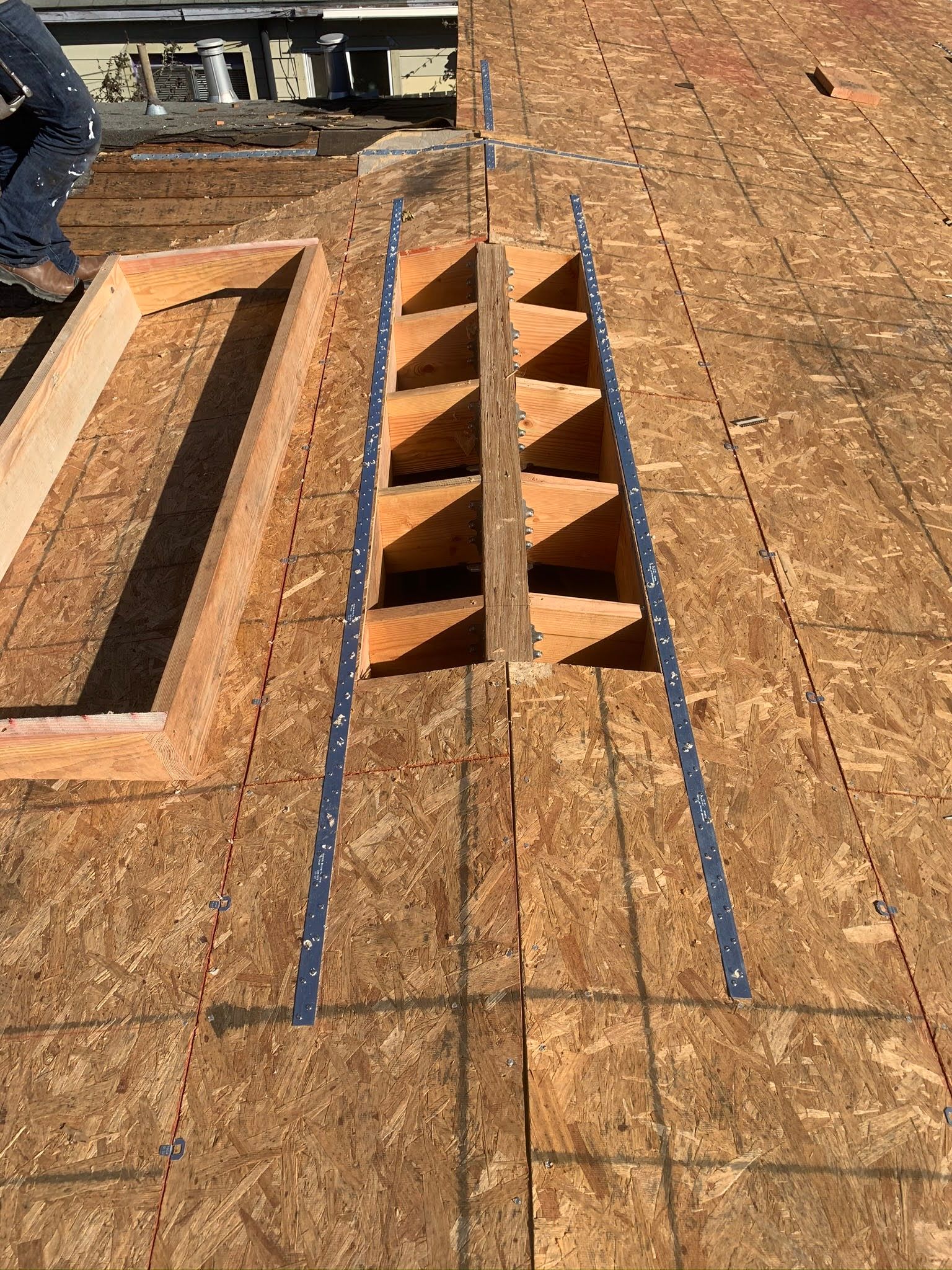 Construction site with wooden floor, rectangular opening, and a narrow orange stairwell framed by blue tape.