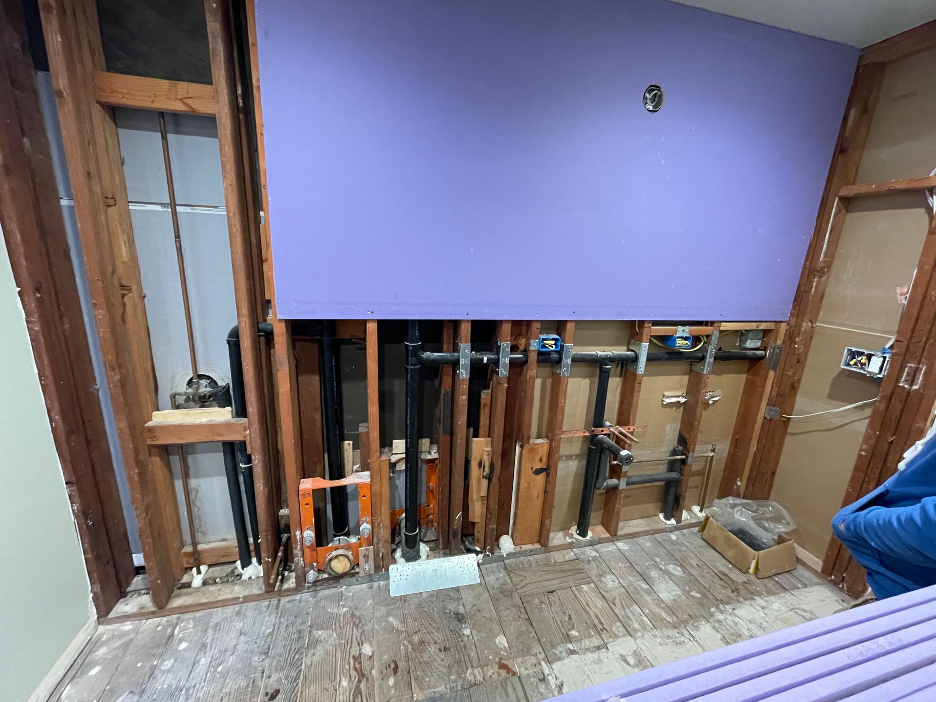 Partially renovated room with exposed wall framing, plumbing, and purple drywall panel