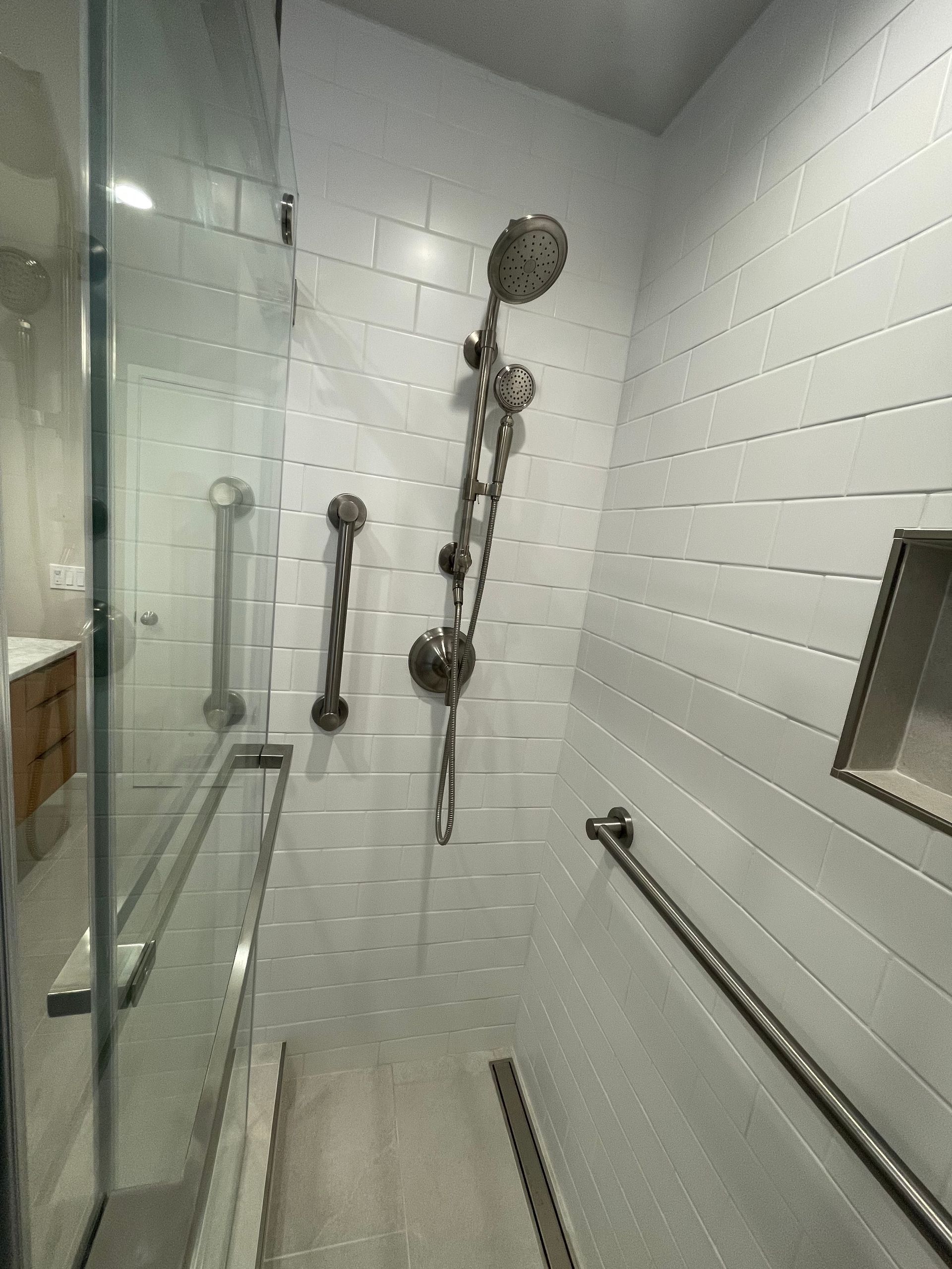 Accessible shower stall with glass door, grab bars, handheld shower, and built-in bench seats