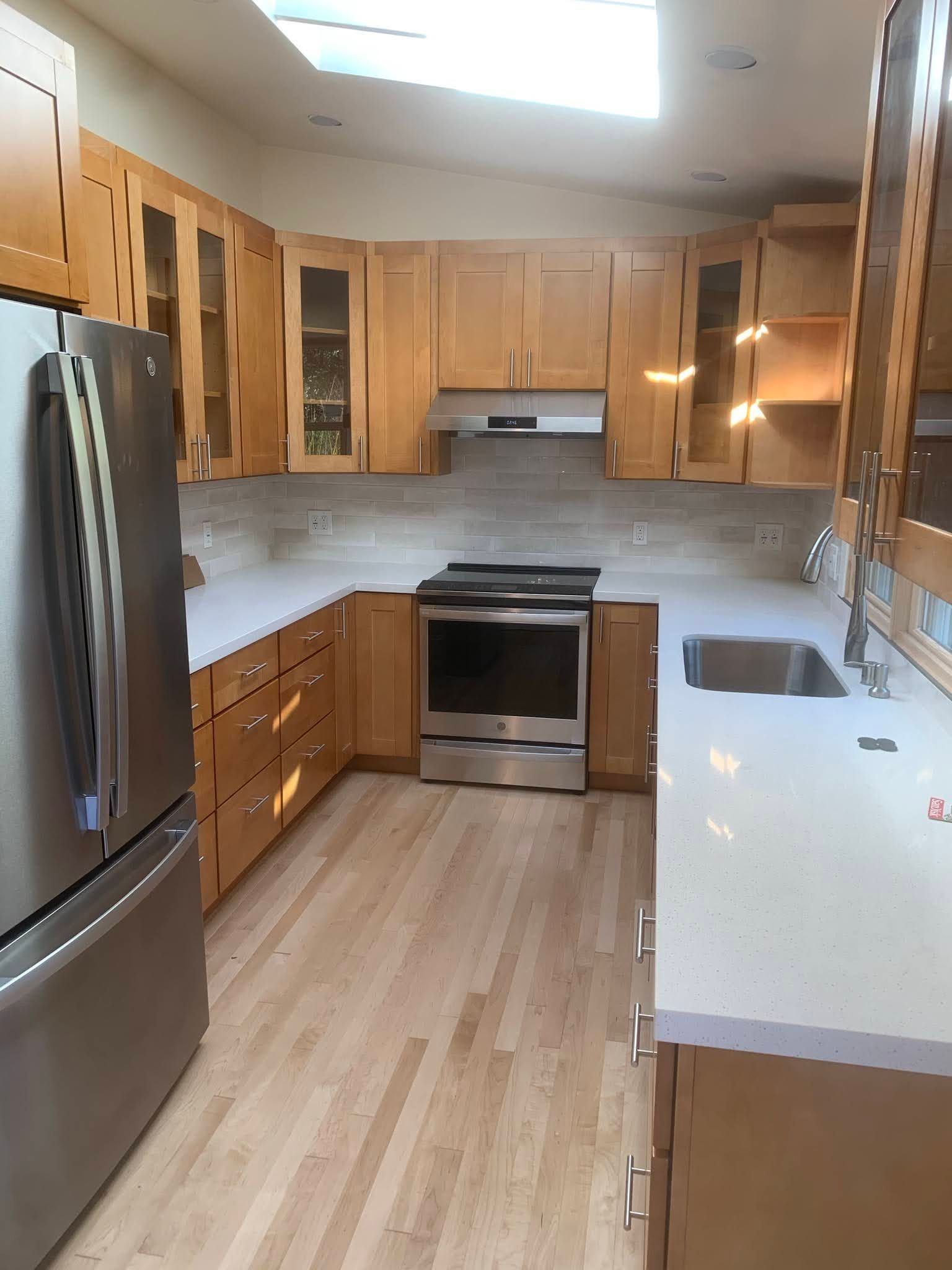 Modern kitchen with stainless steel appliances, wood cabinets, white countertops, and light wood flooring