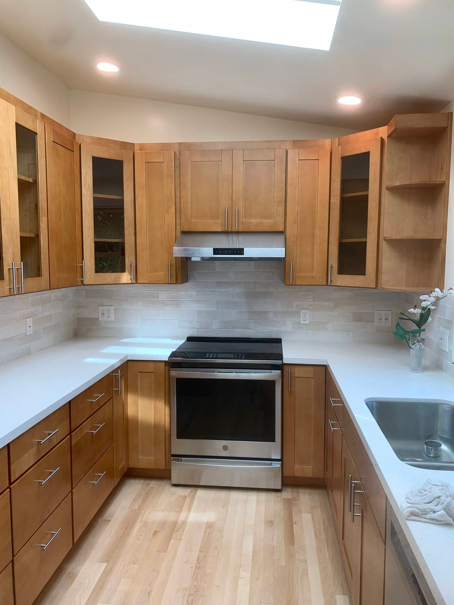 Small galley kitchen with wood cabinets, white countertops, stainless oven, and sink under skylights.