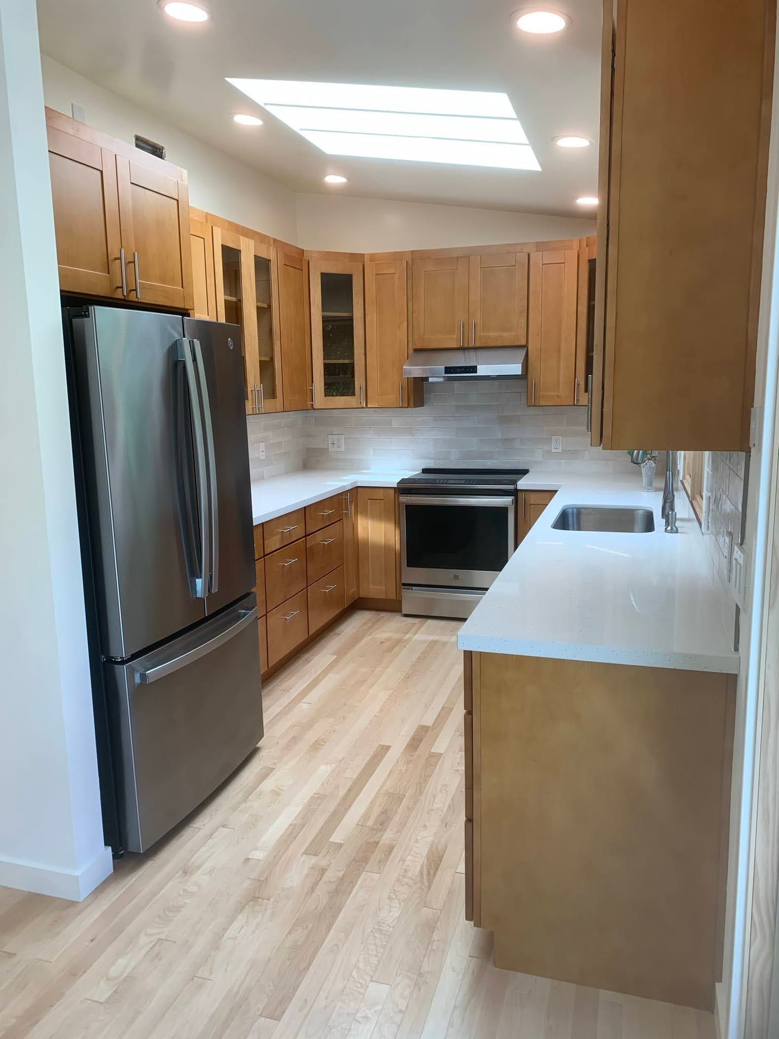 Modern kitchen with stainless steel appliances, light wood cabinets, and a white countertop under skylights