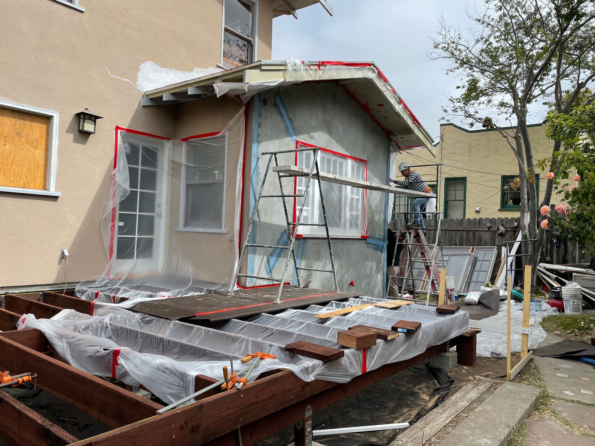 House exterior under renovation with scaffolding and plastic sheeting around a porch