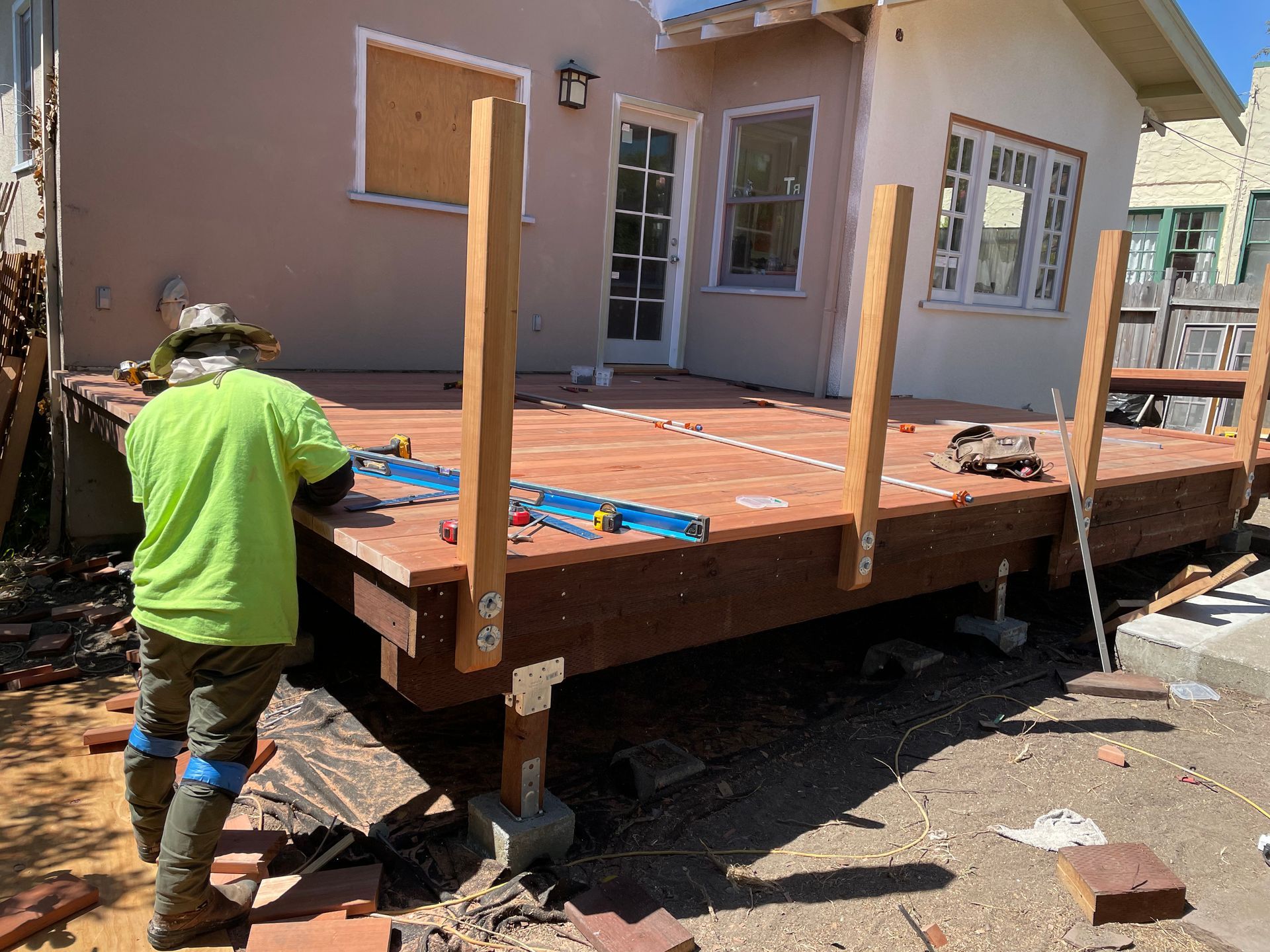 Worker building a wooden deck on a house under construction, with support posts and tools visible