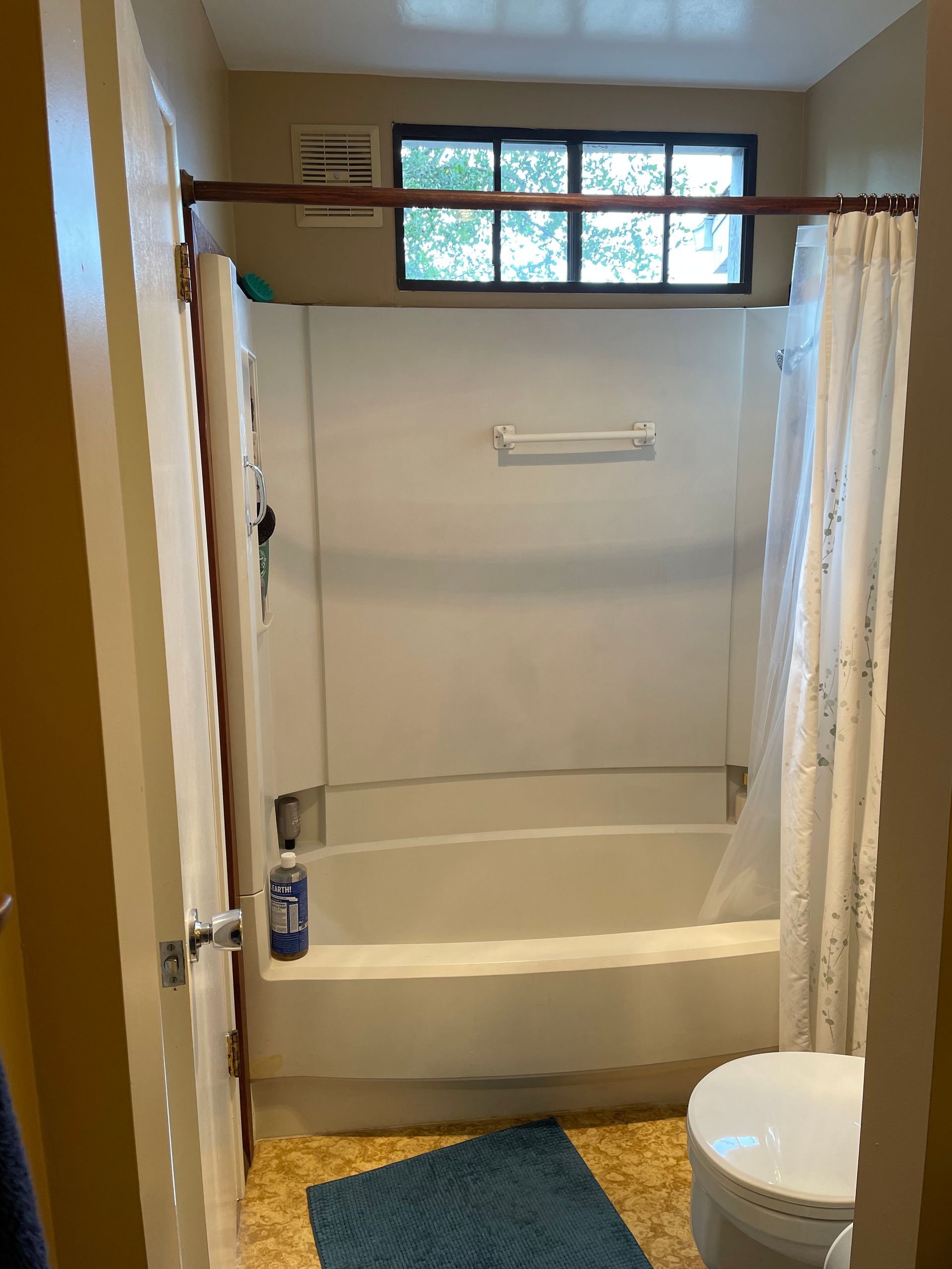 Accessible bathroom with a tub shower, grab bars, and a toilet beside a blue bath mat.