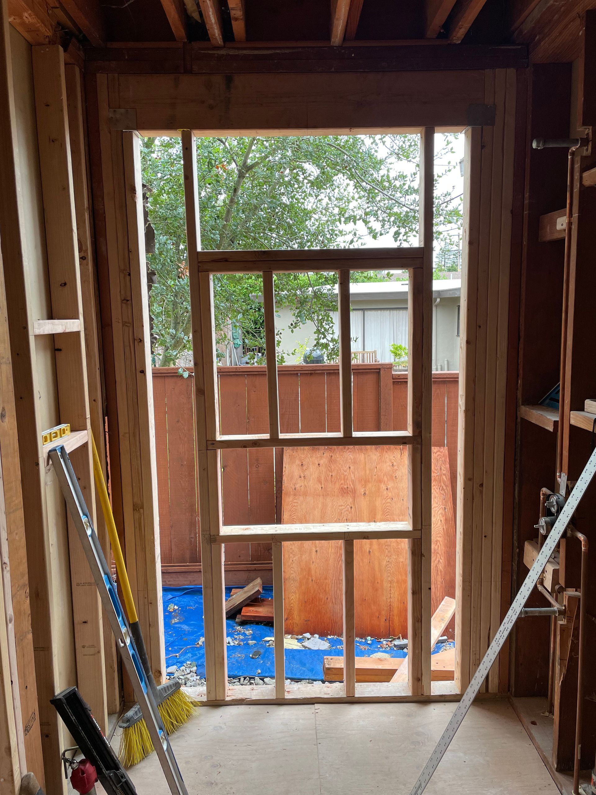 Unfinished doorway framing with exposed wood studs, looking out to a fenced backyard.