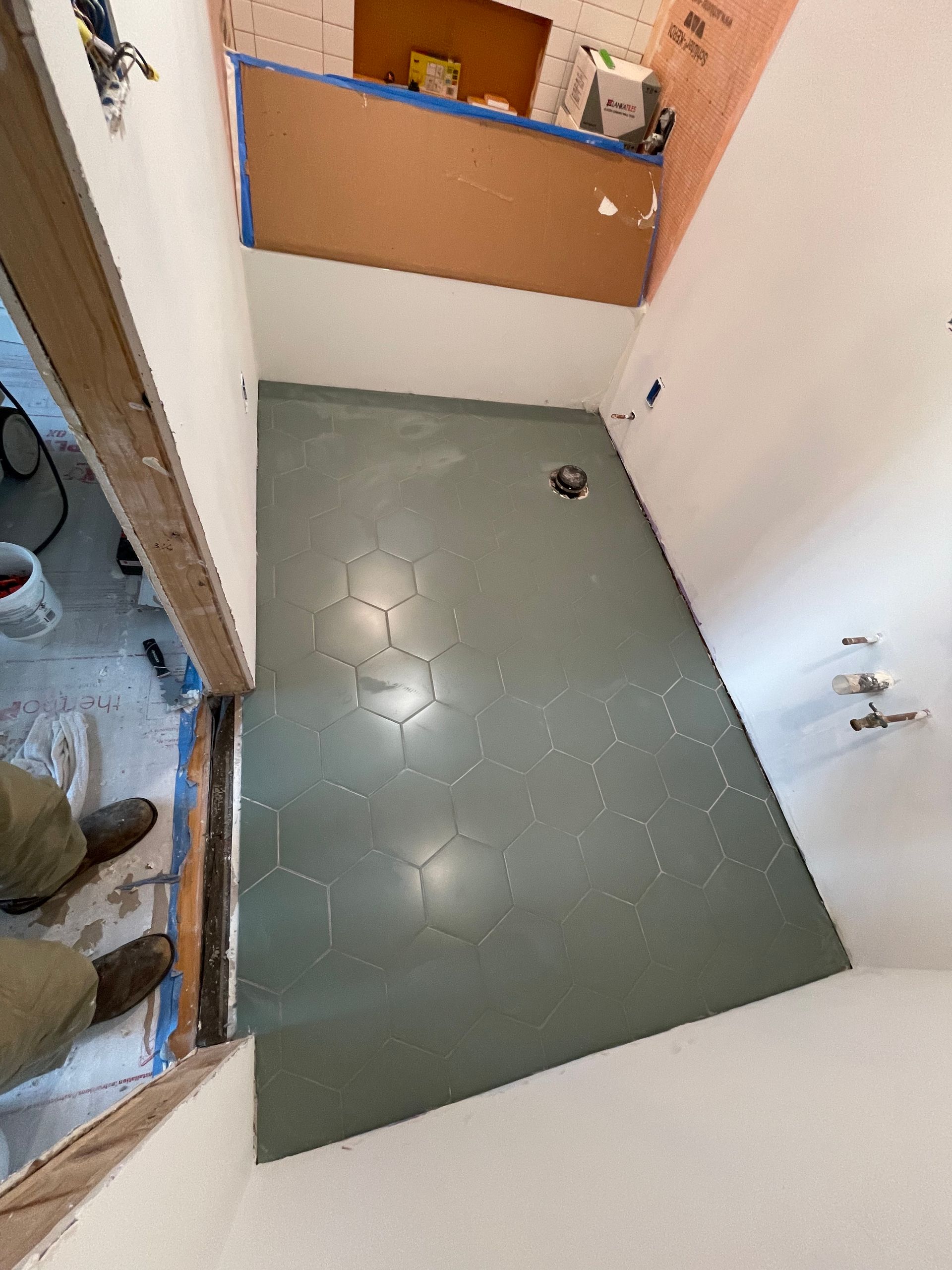 Small bathroom with green tiled floor, white walls, and a wooden cabinet over the toilet area.