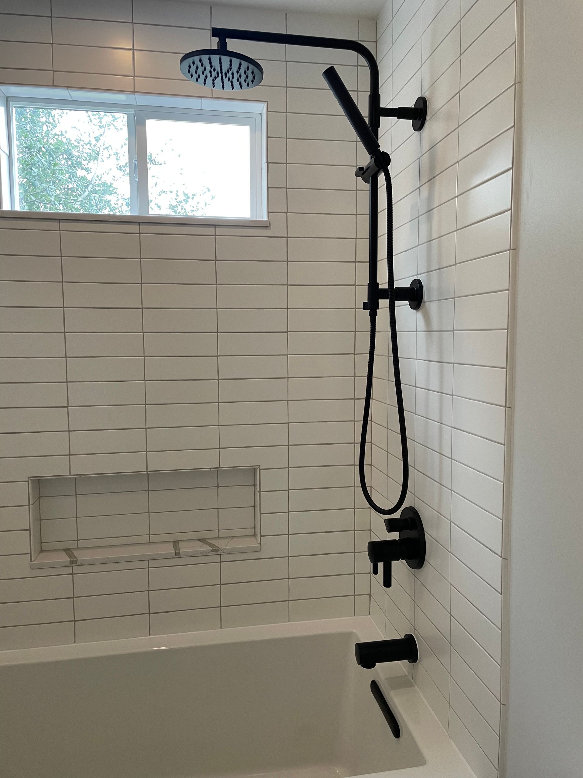 Accessible bathroom shower with grab bar, handheld showerhead, and bench by a window