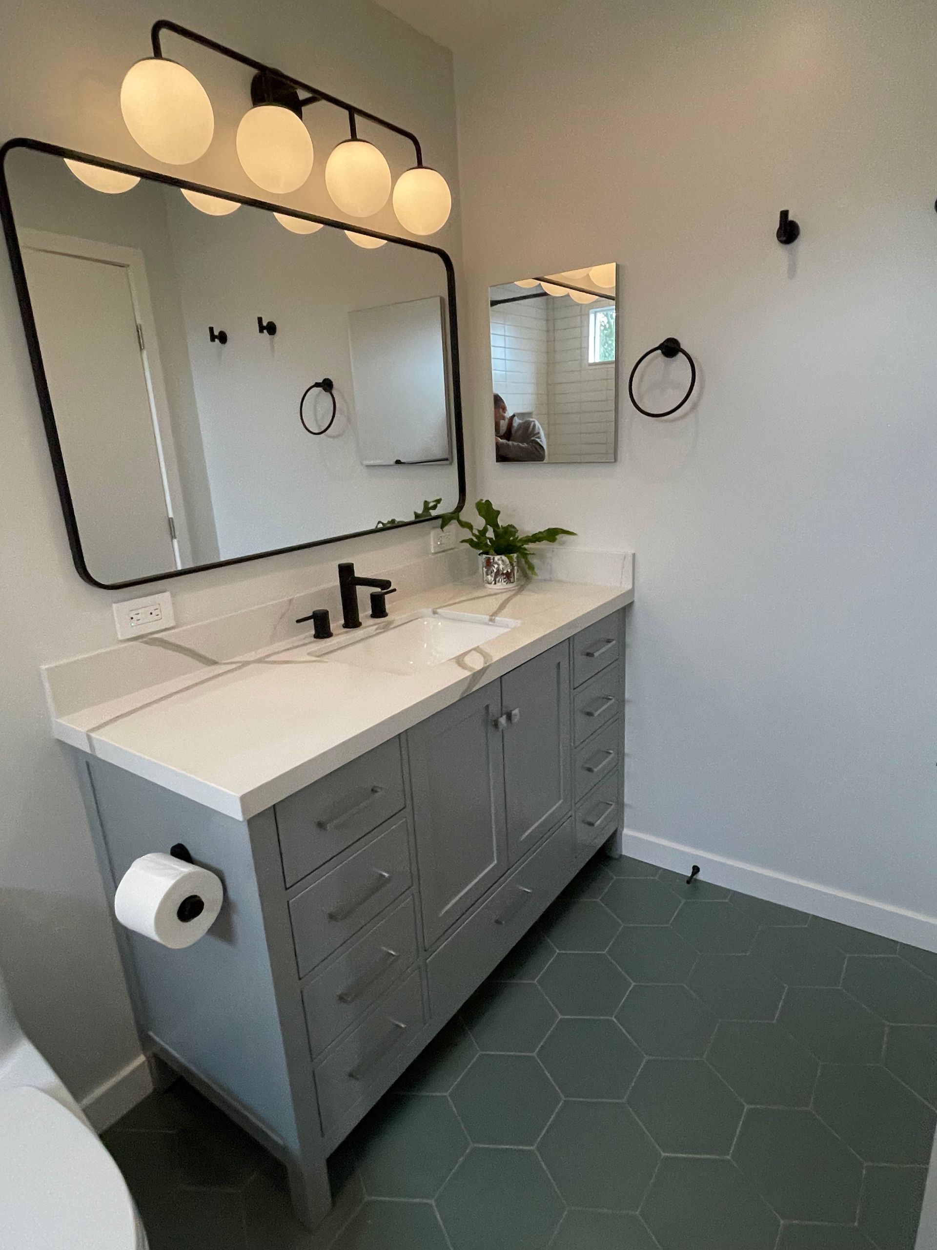 Modern bathroom vanity with large mirror, wall lights, gray cabinets, and green hex tile floor