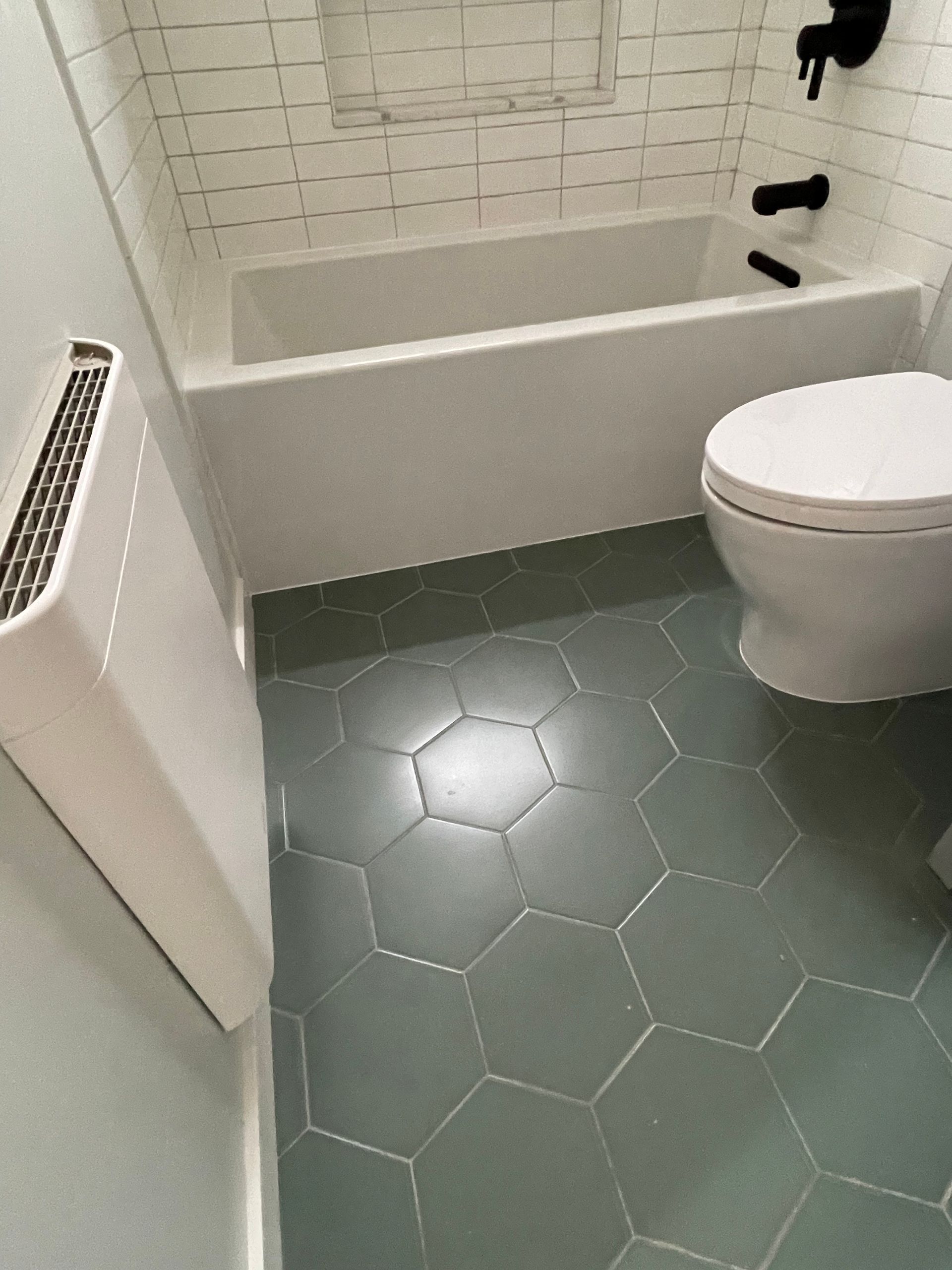 Small bathroom with white tub and toilet, green hex tile floor, and wall radiator.