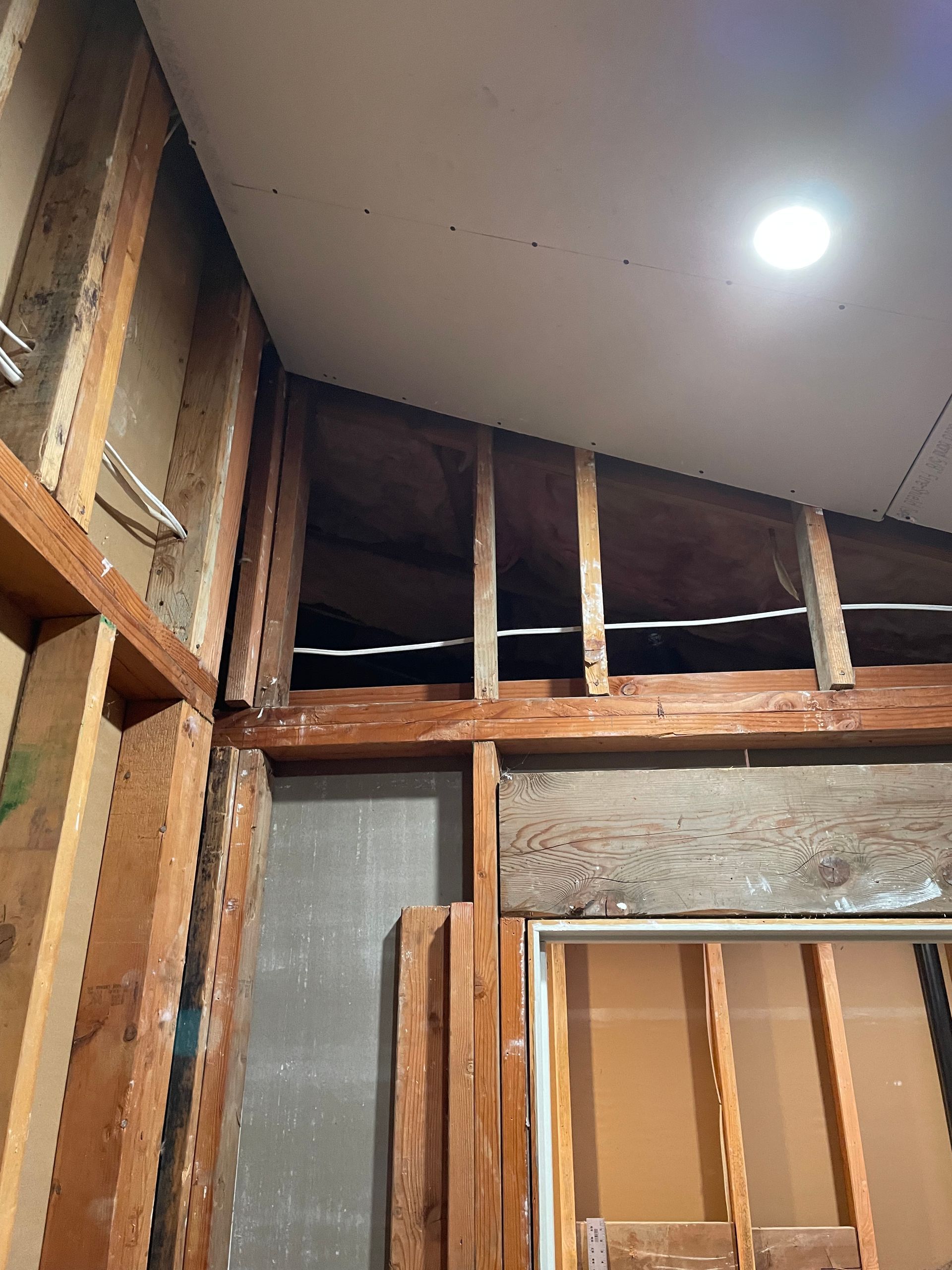 Interior wall exposed to studs and insulation, with a ceiling light and a doorway frame under construction