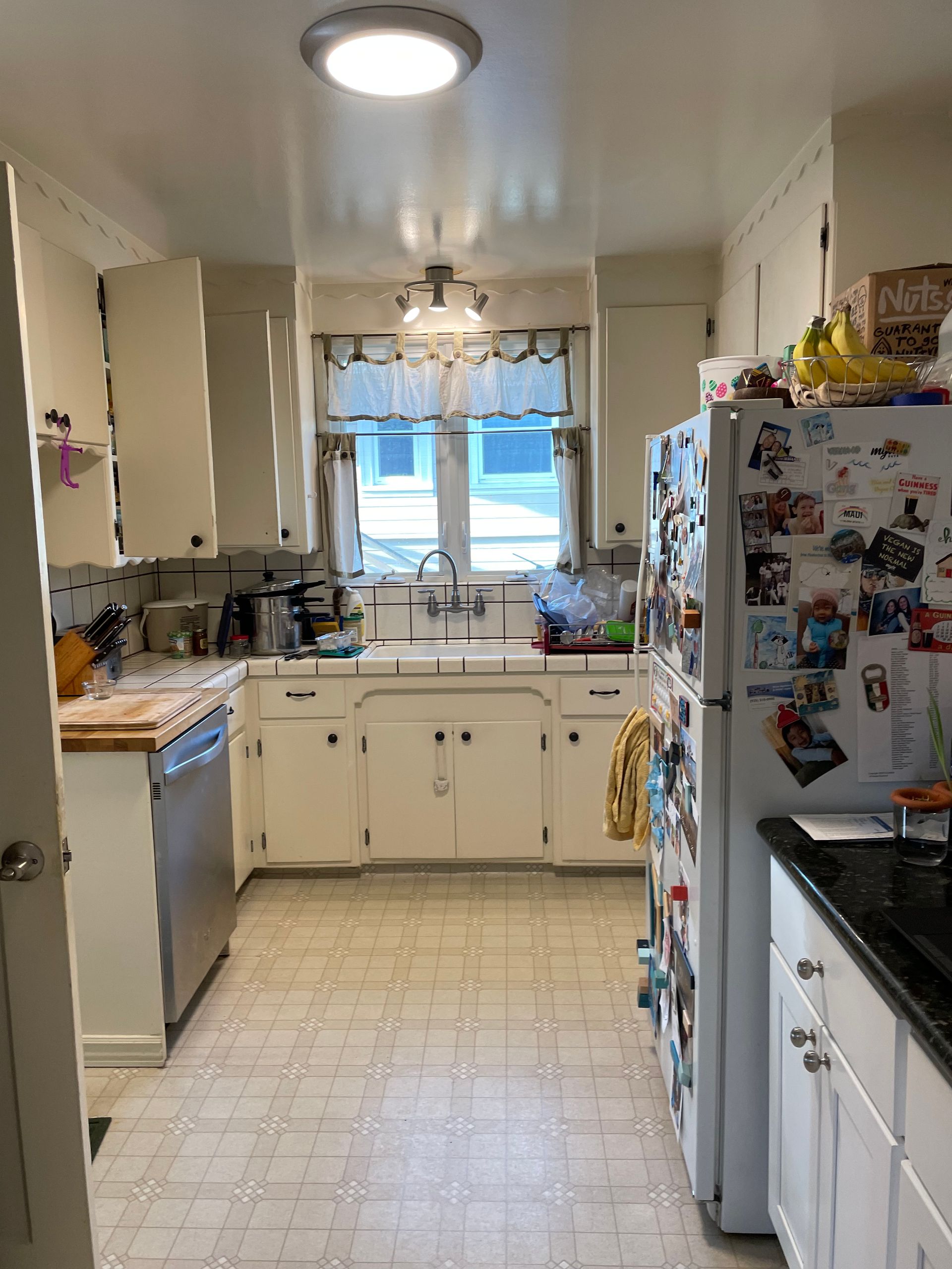 Bright kitchen with white cabinets, tiled floor, and a refrigerator covered in magnets.