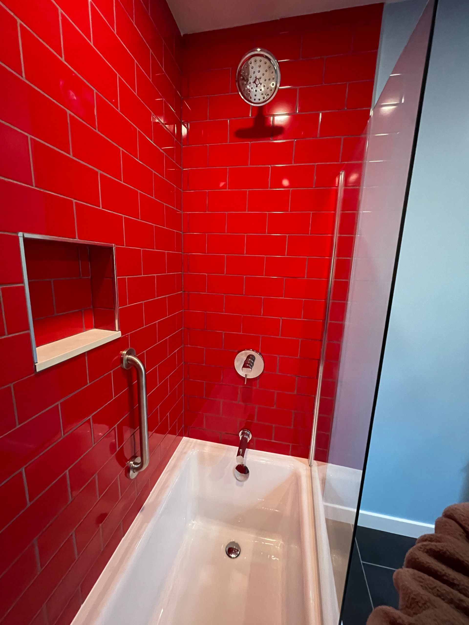 Red-tiled shower-tub with chrome fixtures and frosted glass door in a bathroom