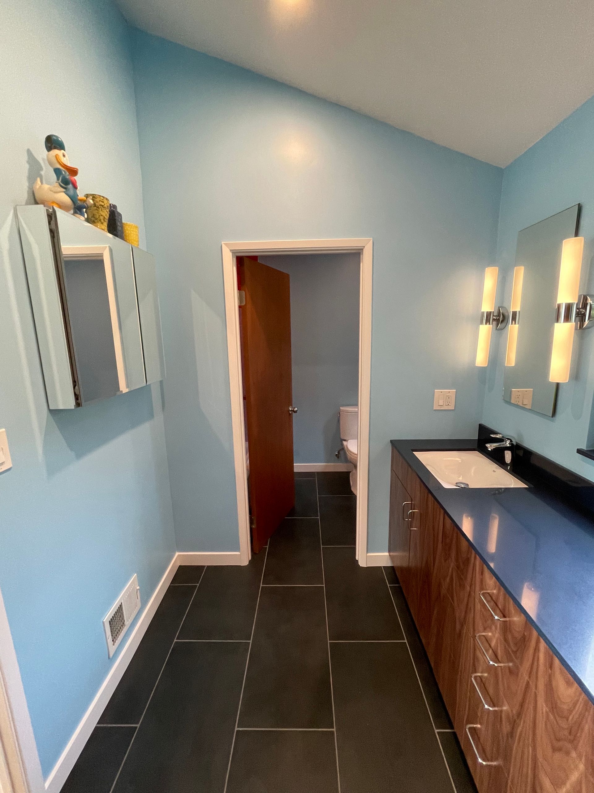 Blue bathroom with double vanity, dark tile floor, and open doorway