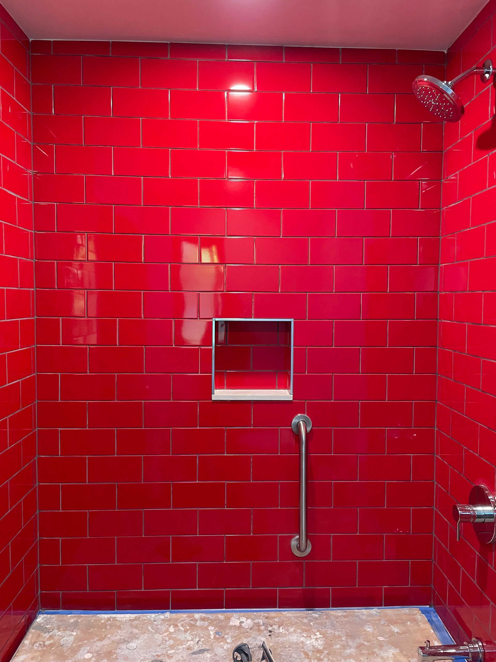 Red-tiled shower stall with grab bar, built-in shelf, and chrome showerhead.