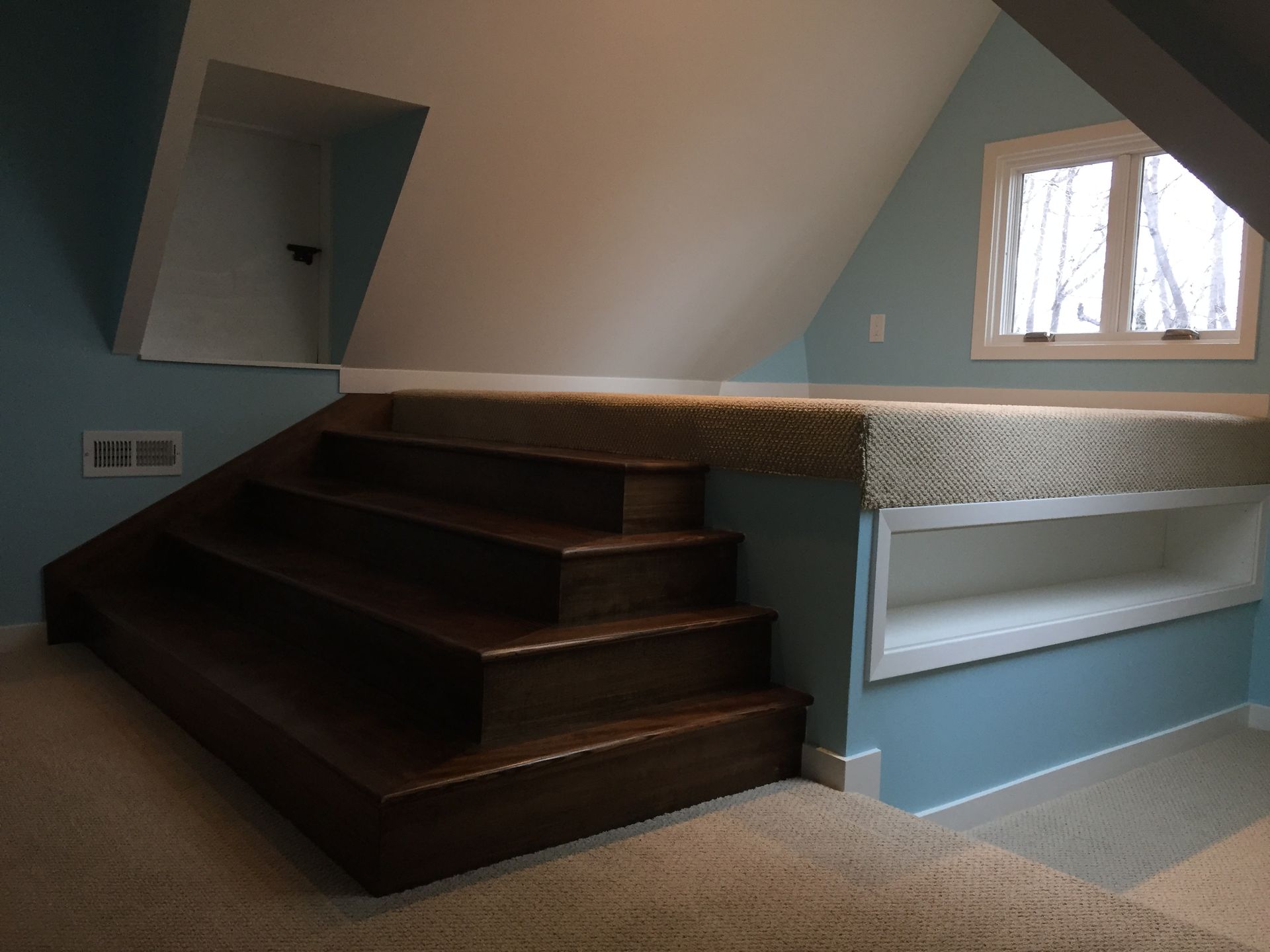 Attic room with dark wooden stairs, blue walls, and a small window