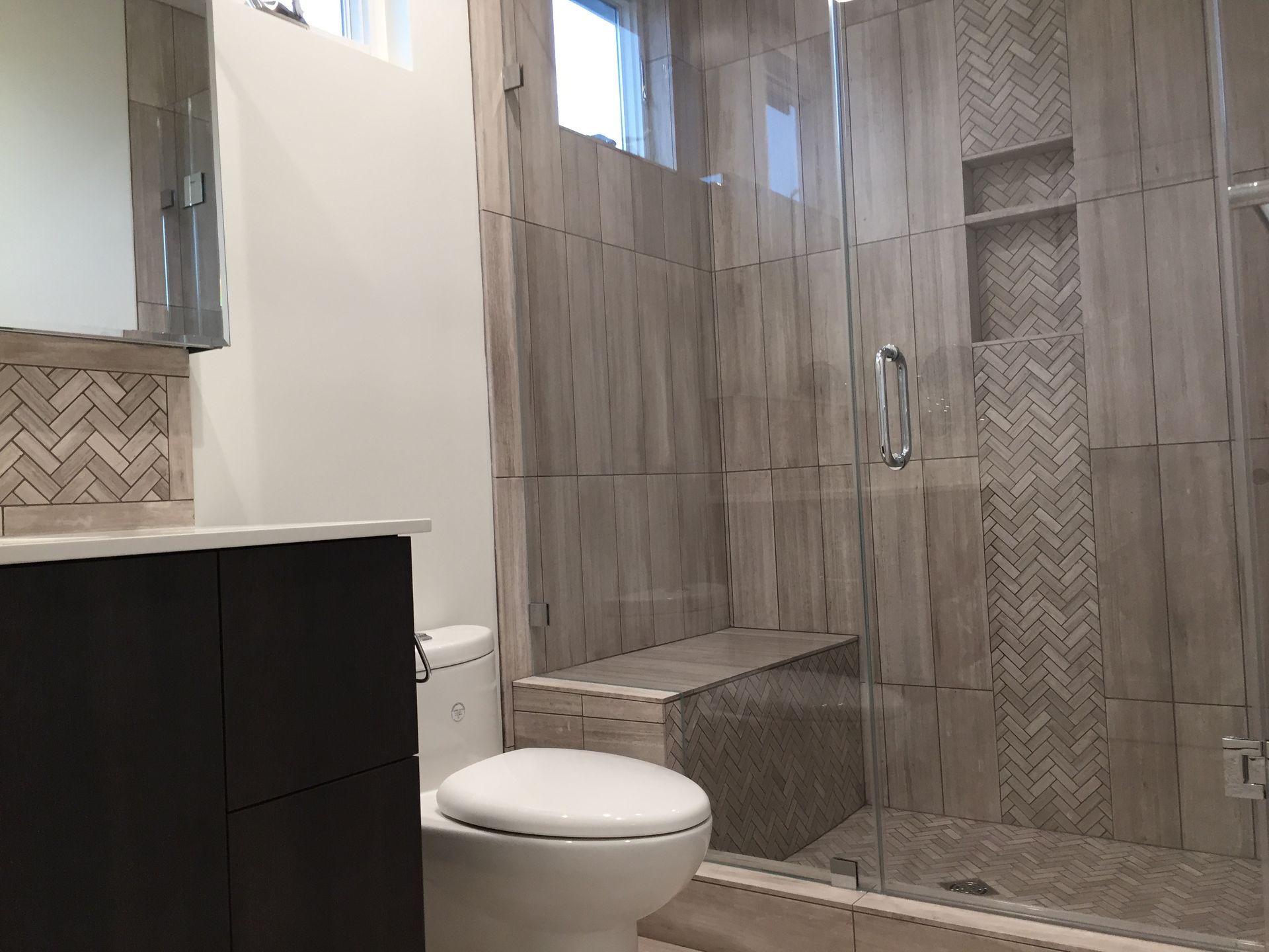 Modern bathroom with glass shower, toilet, and dark vanity in gray tile finishes