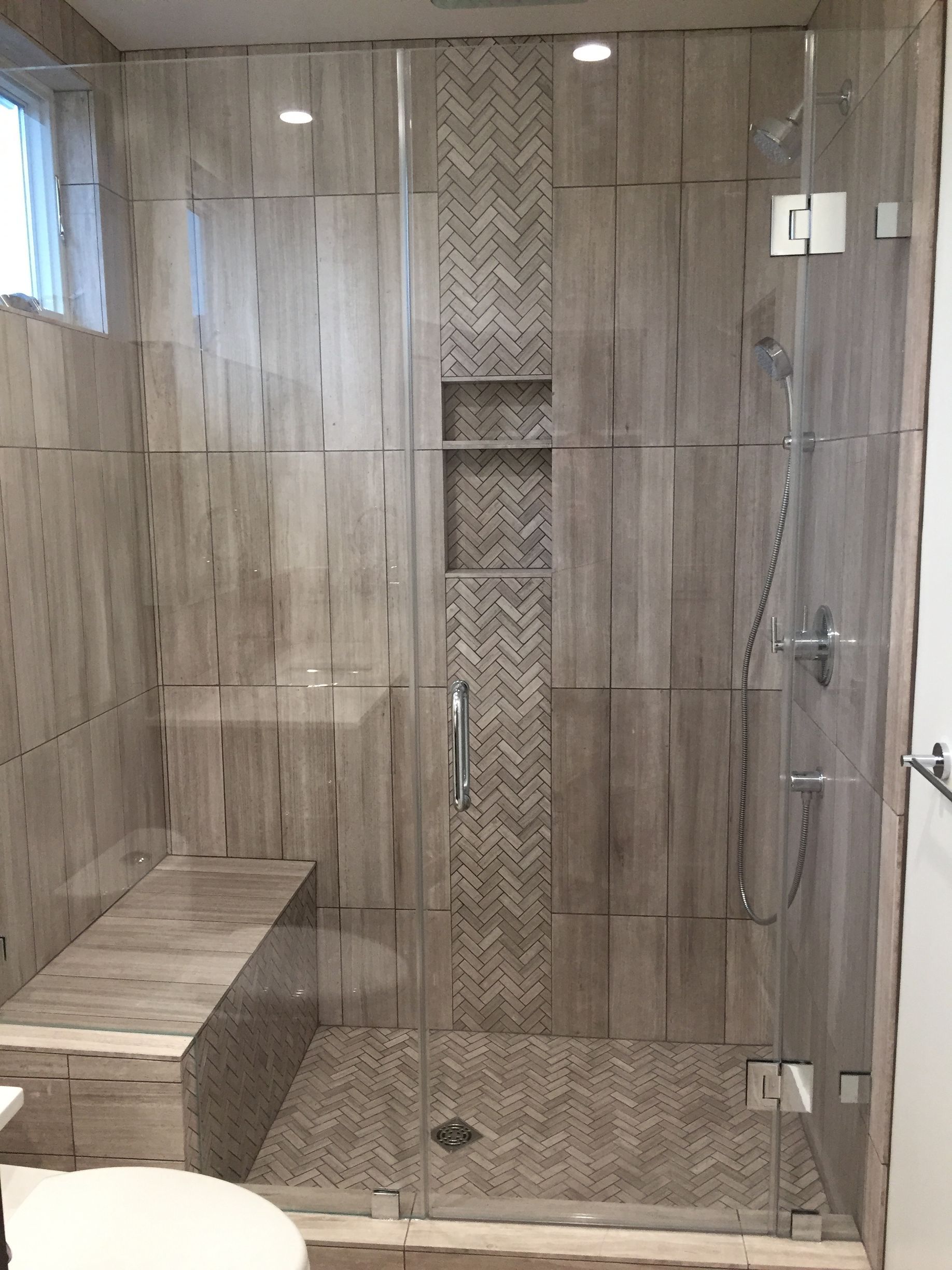 Modern glass shower with beige tile, built-in bench, and patterned accent wall.
