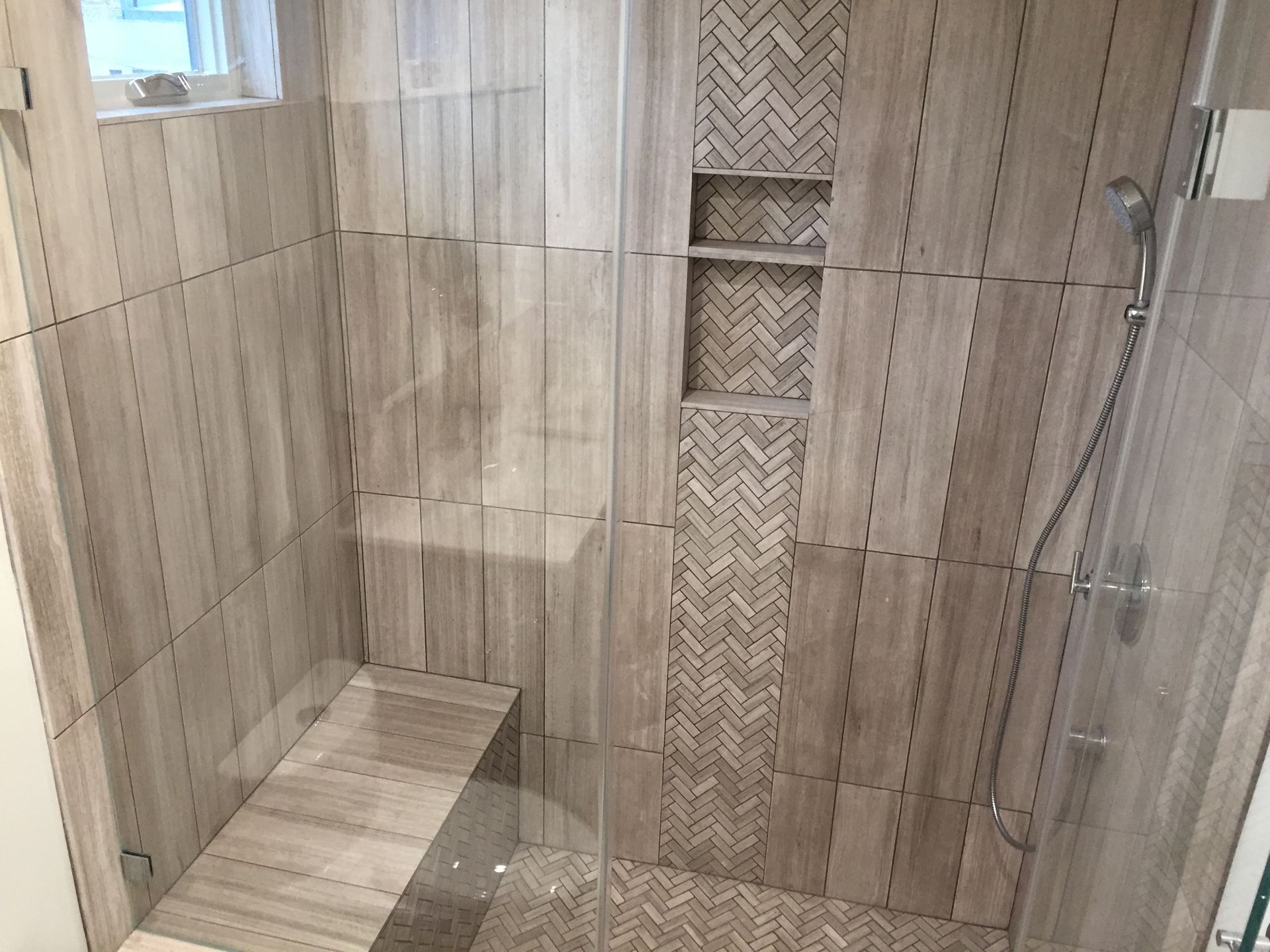 Modern tiled shower with glass enclosure, built-in bench, and recessed shelf.