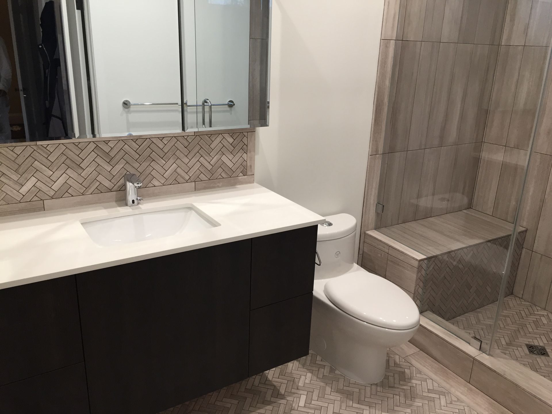 Modern bathroom with dark vanity, white sink, toilet, mirror, and tiled walk-in shower