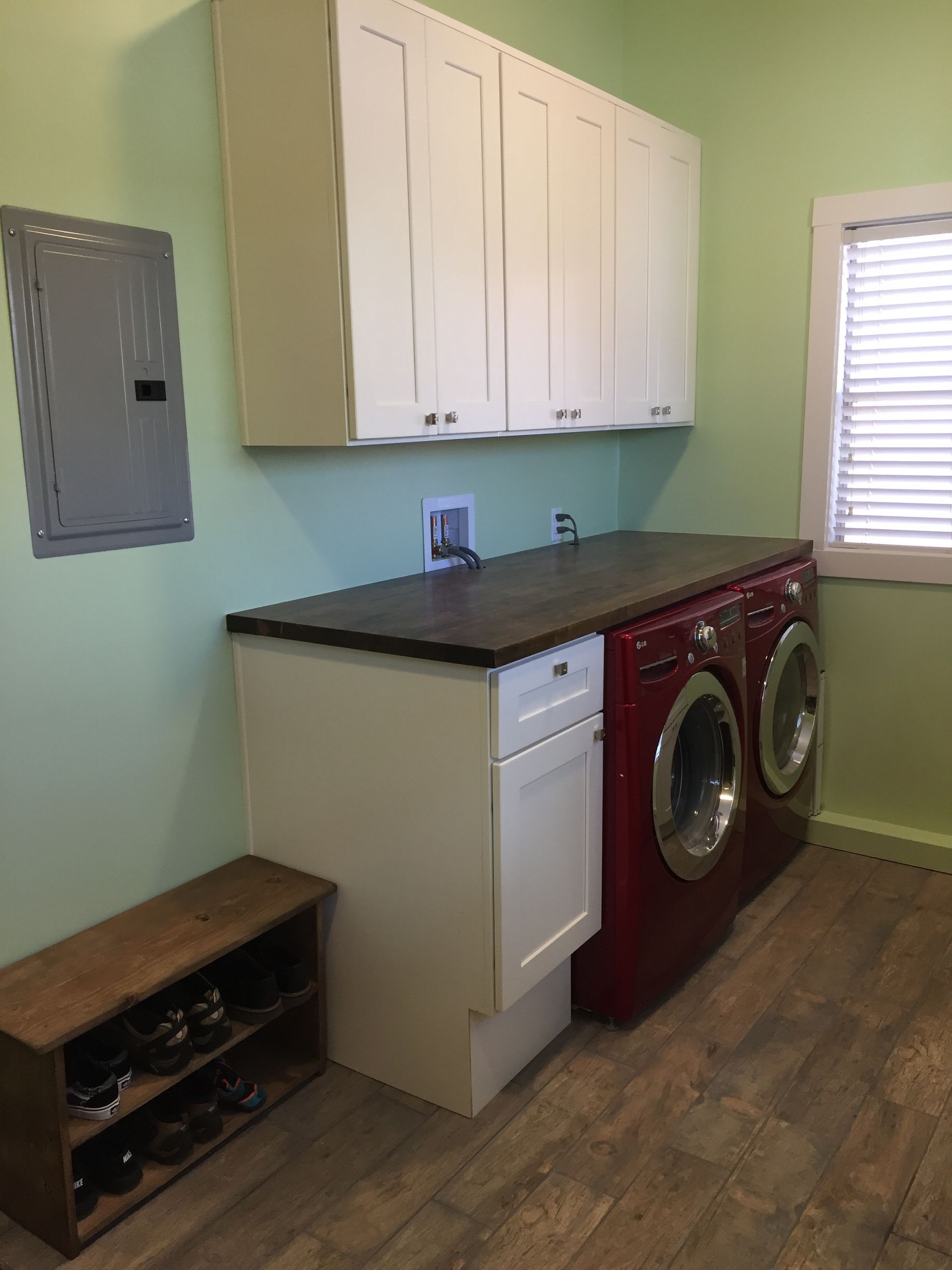 Laundry room with stacked washer and dryer, white cabinets, and a dark countertop on mint green walls.