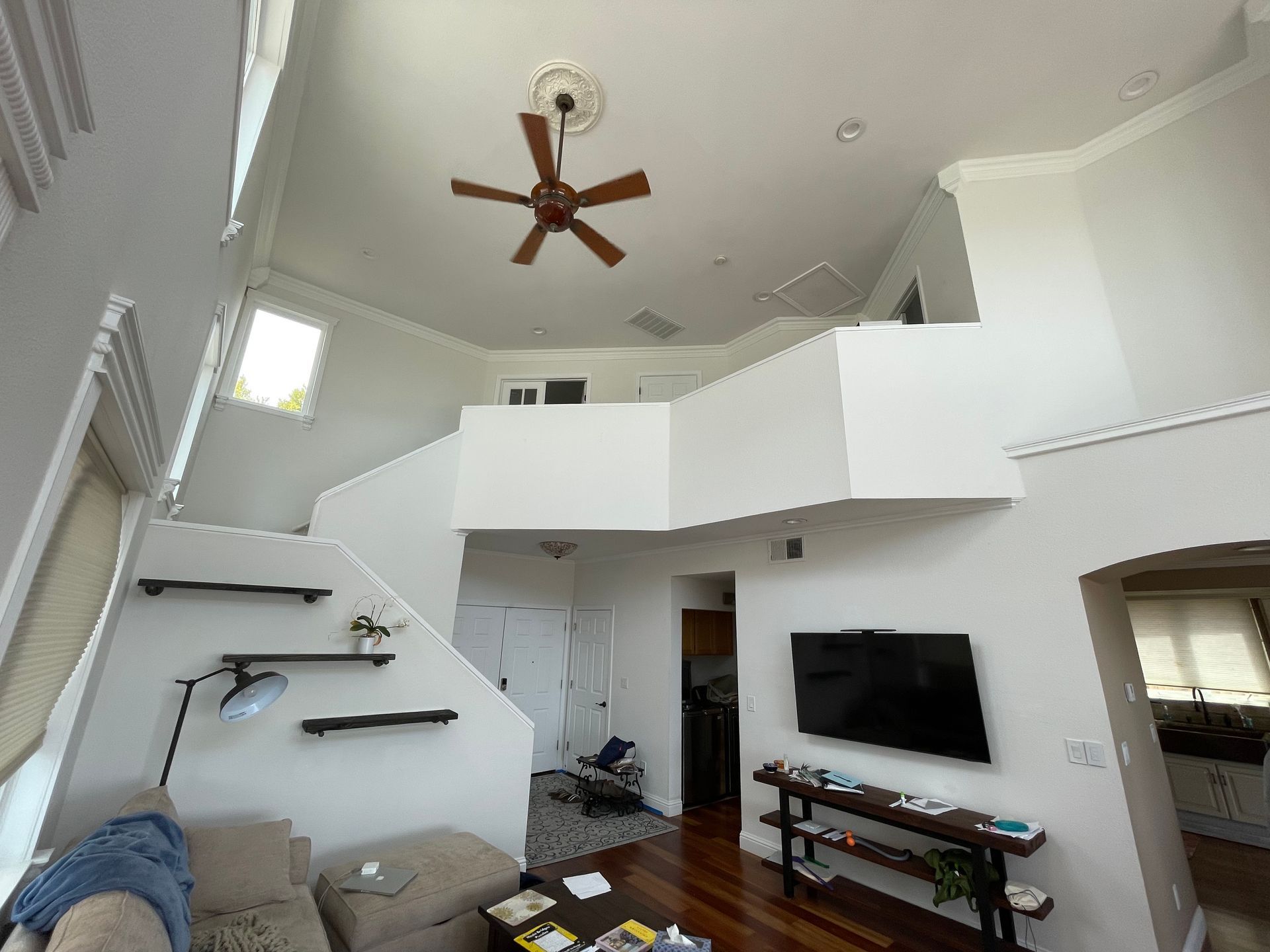 Modern living room with high ceiling, ceiling fan, wall-mounted TV, staircase, and loft area