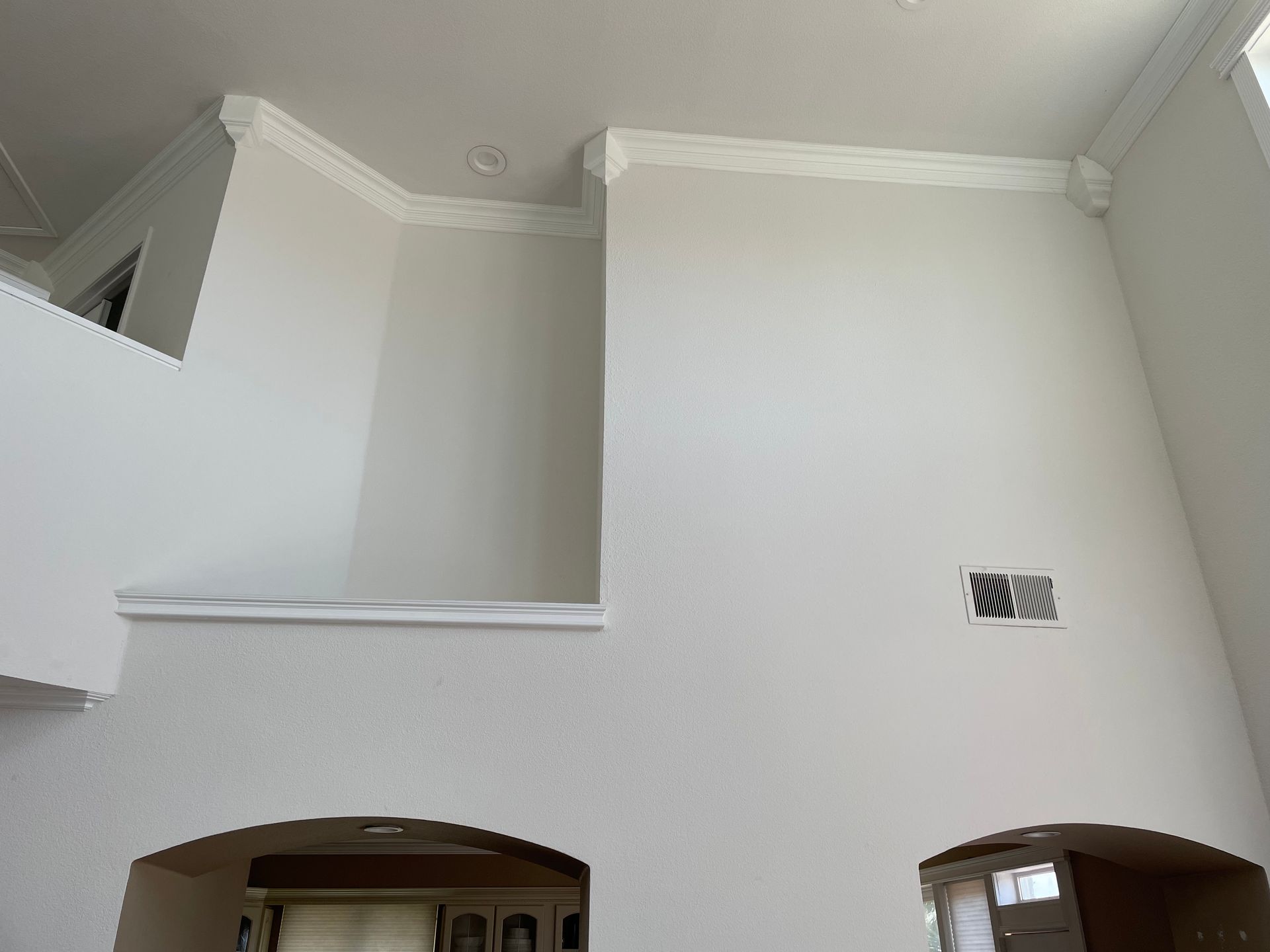 Interior with high white walls, crown molding, and two arched doorways below a small vent.