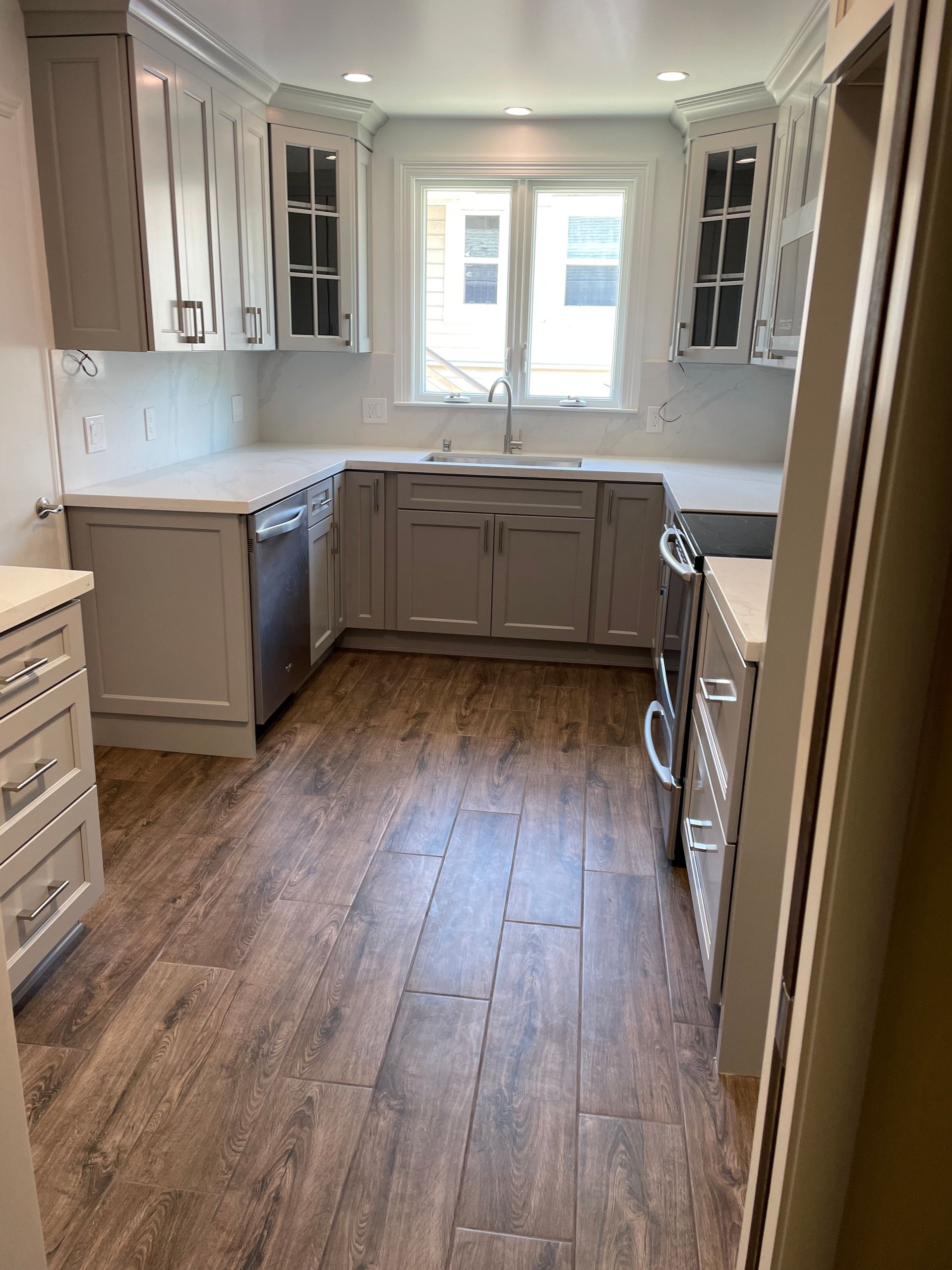 Bright remodeled kitchen with gray cabinets, wood floor, and a window over the sink