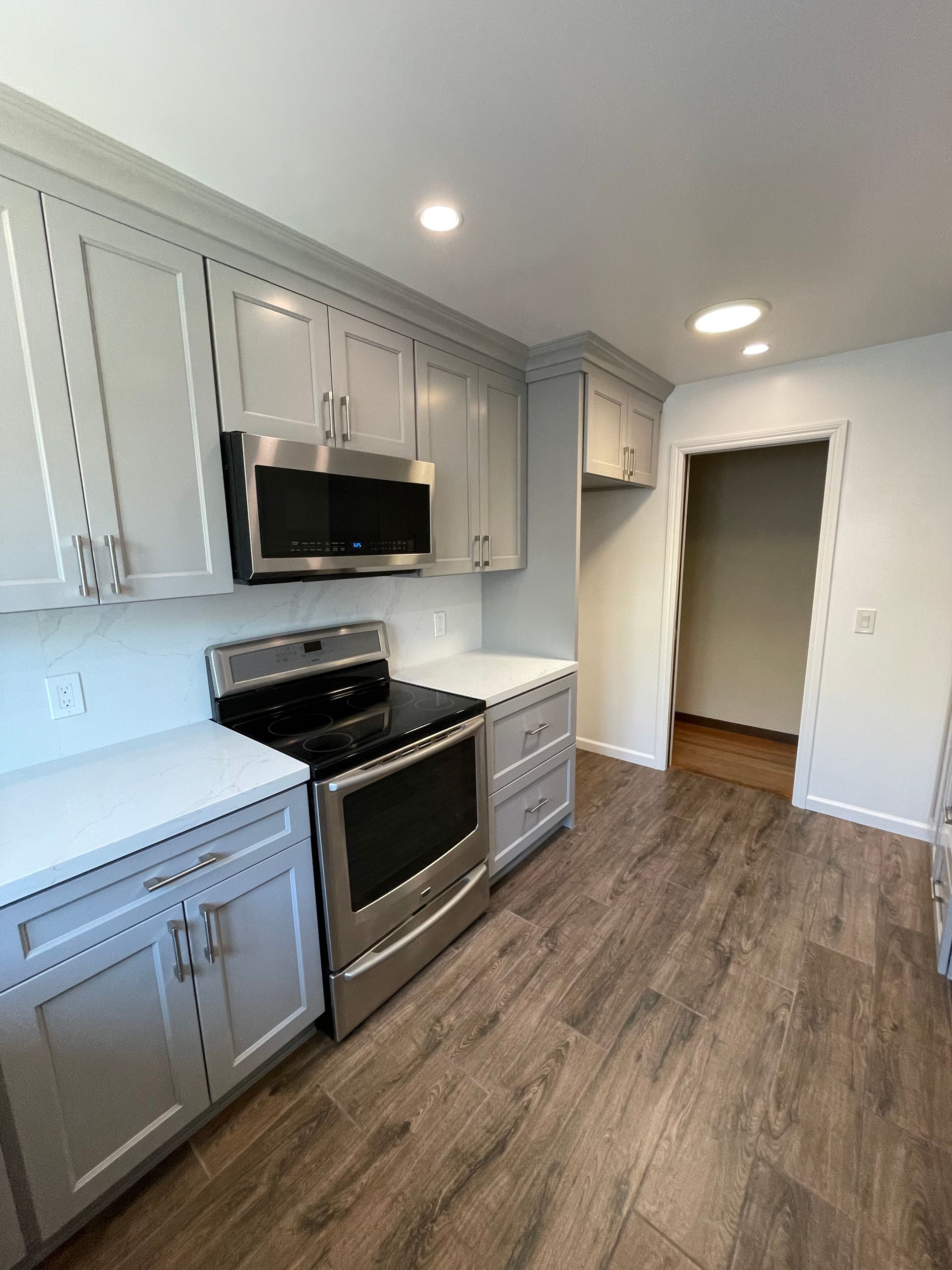 Bright modern kitchen with white cabinets, stainless stove, and wood-look flooring
