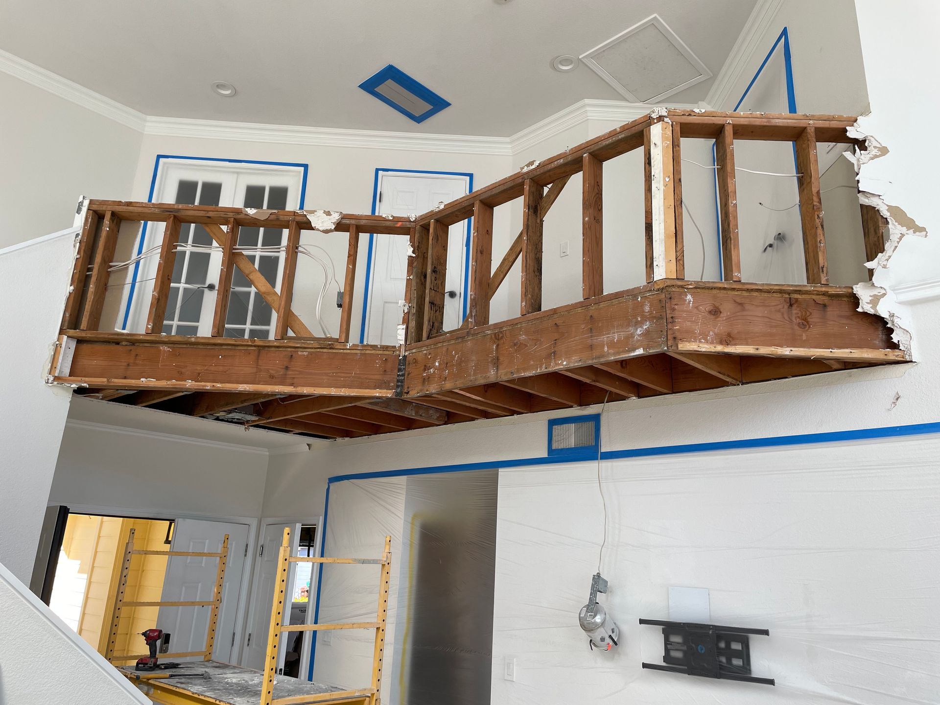 Wooden mezzanine under construction in a white room, with blue painter’s tape and scaffolding below.