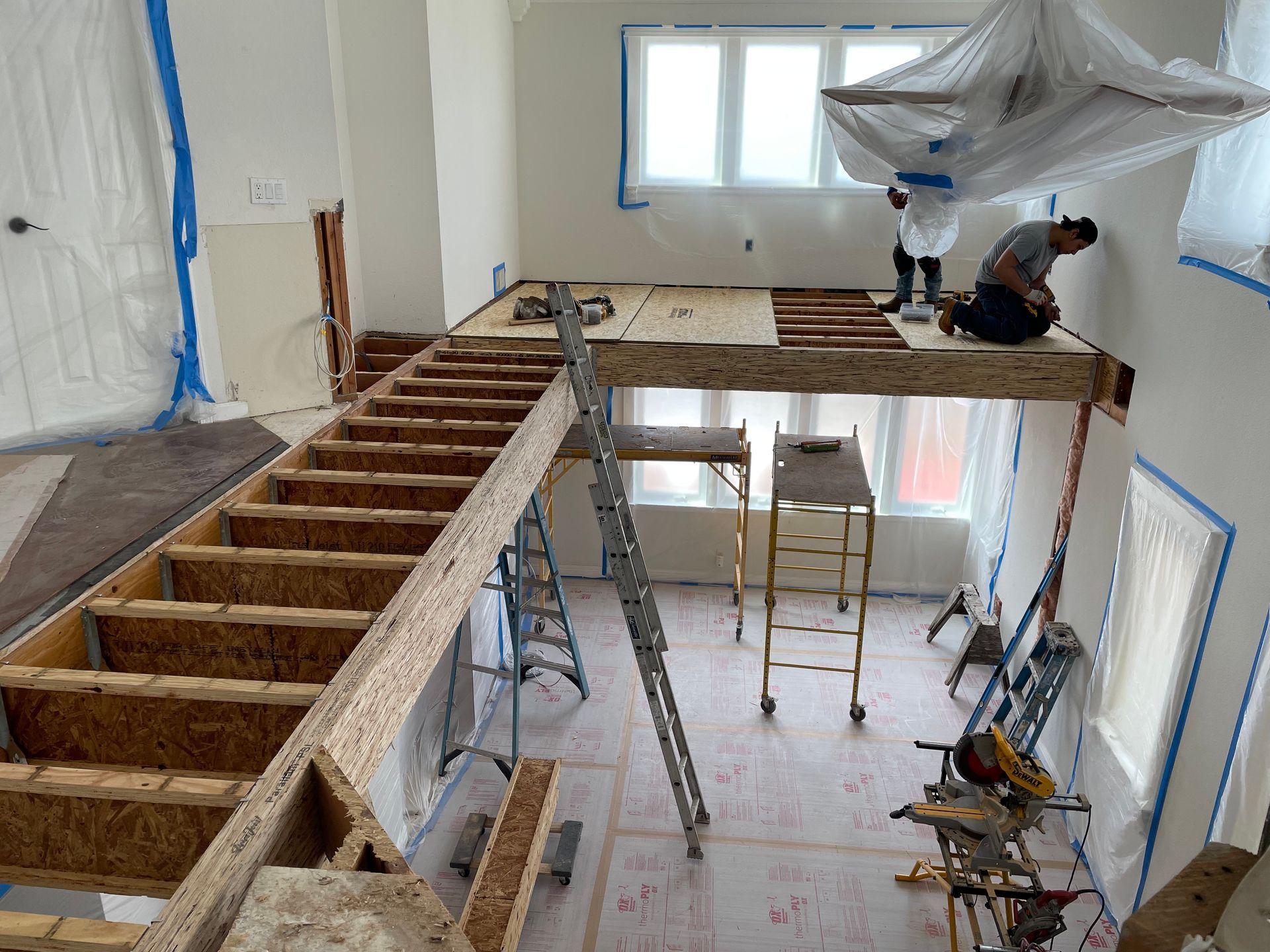Indoor construction site with workers building a lofted mezzanine and ladder in a high-ceiling room