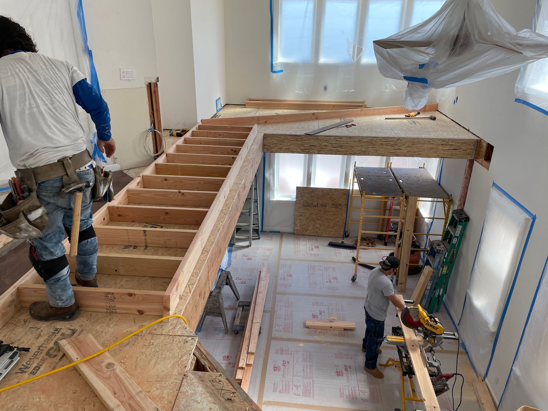 Workers building a wooden loft frame inside a bright room under renovation