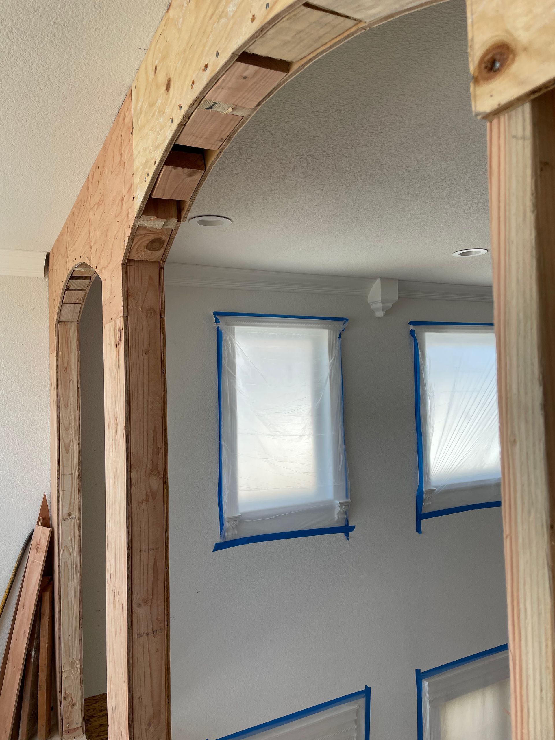 Curved unfinished wooden archway overlooking a room with taped-off windows and gray walls