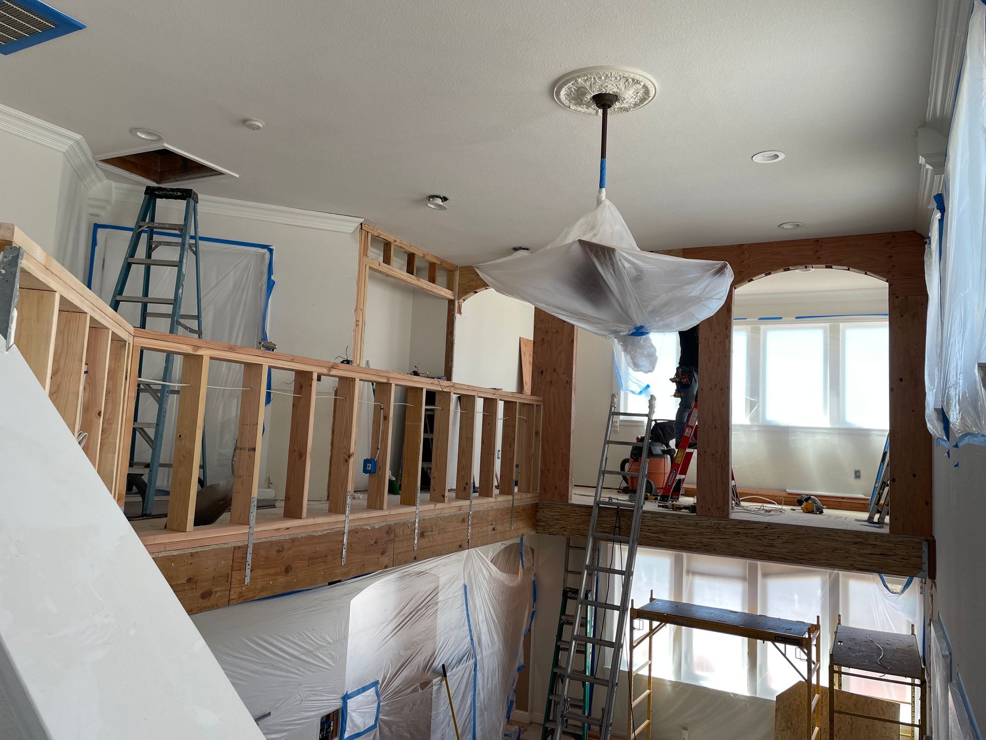 Partially renovated room with exposed framing, ladders, and plastic-covered light fixture