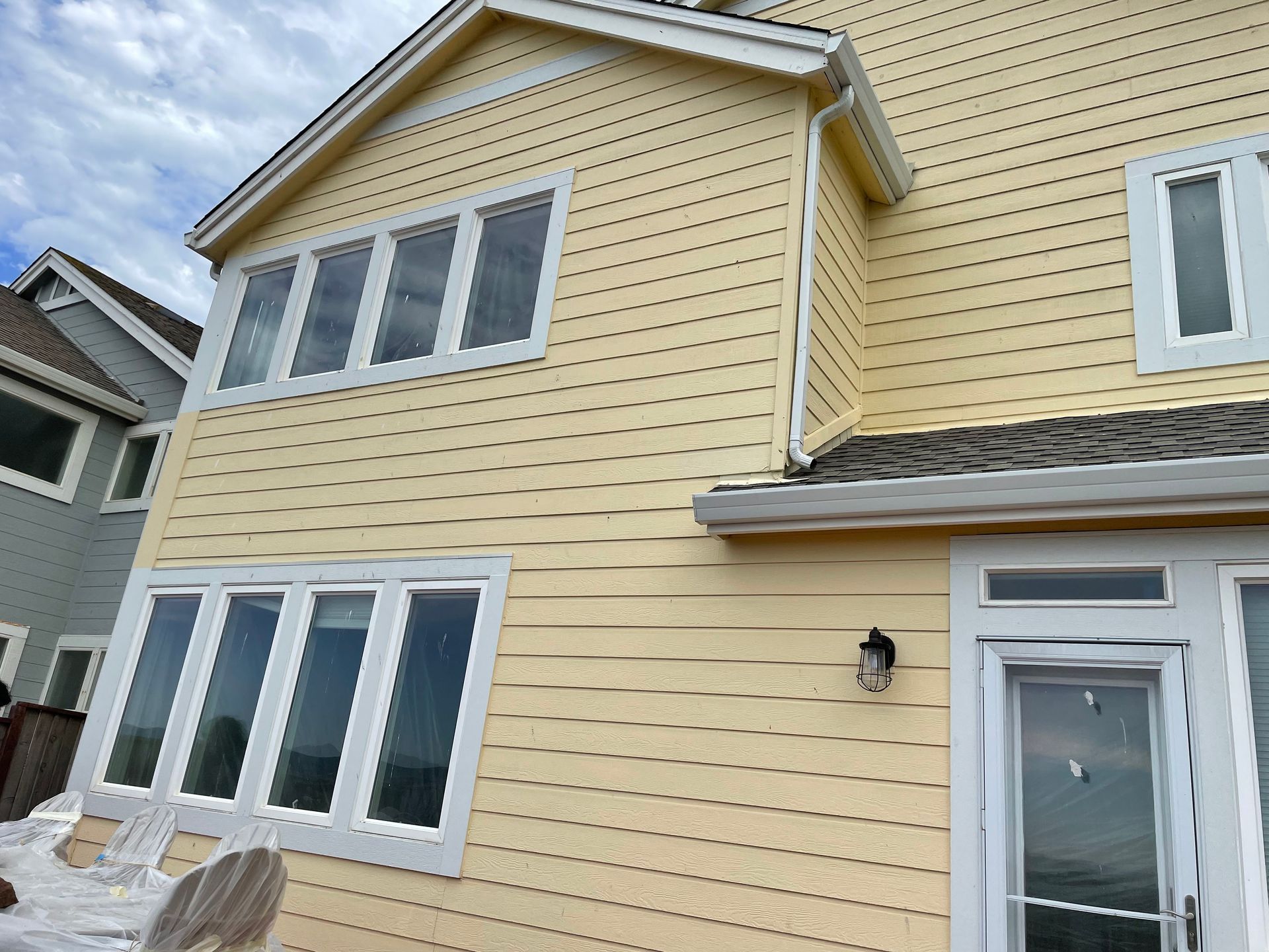 Yellow two-story house exterior with white-trimmed windows and a gray roof, viewed from below