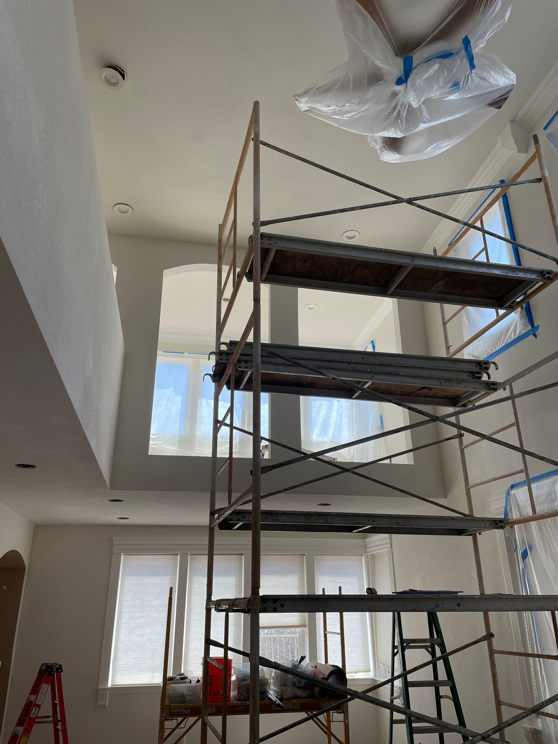 Scaffold and covered ceiling work area inside a room with white walls and a window.