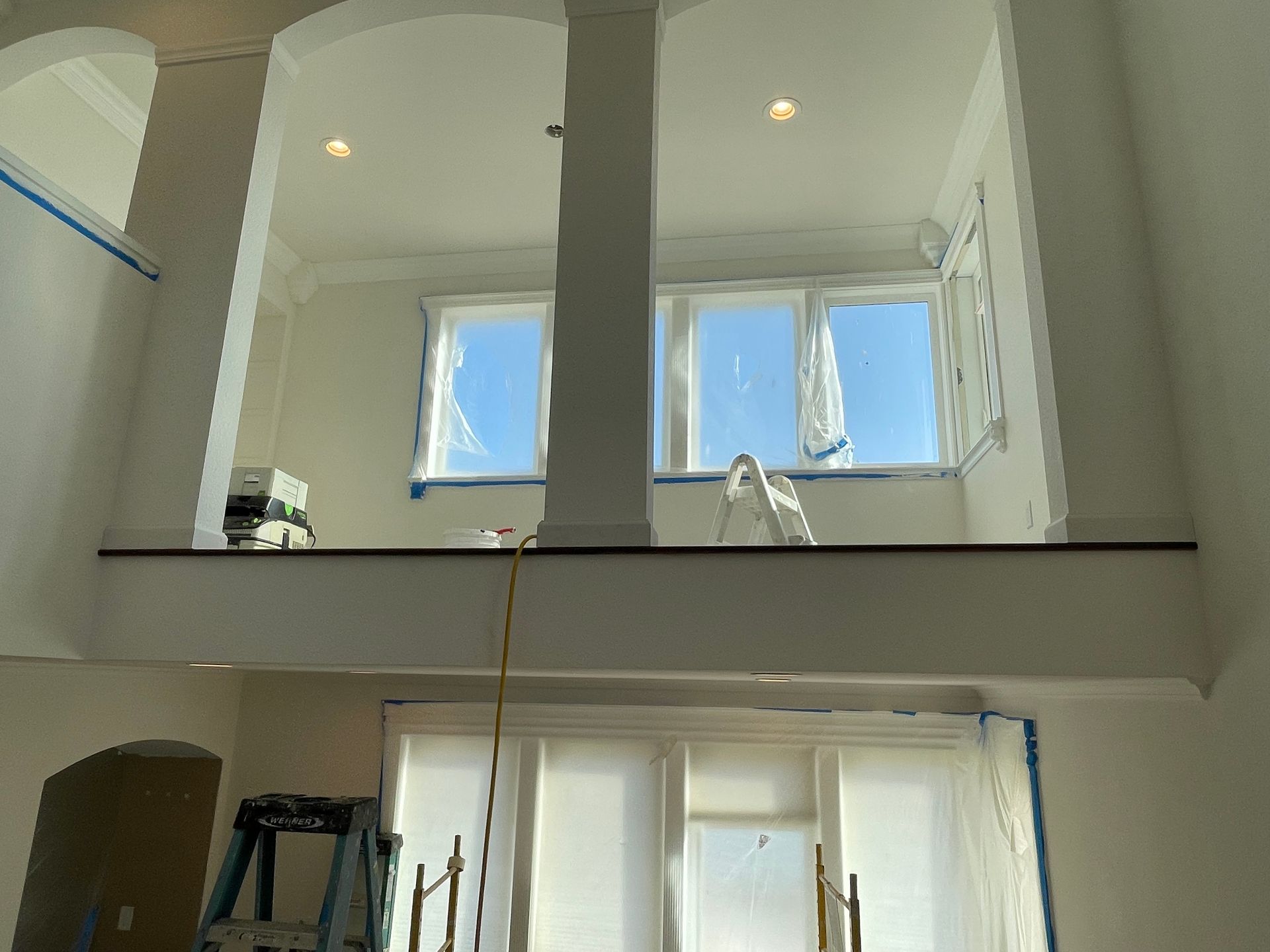 Bright white interior with two tall windows, recessed lights, and a ladder on the lower level.