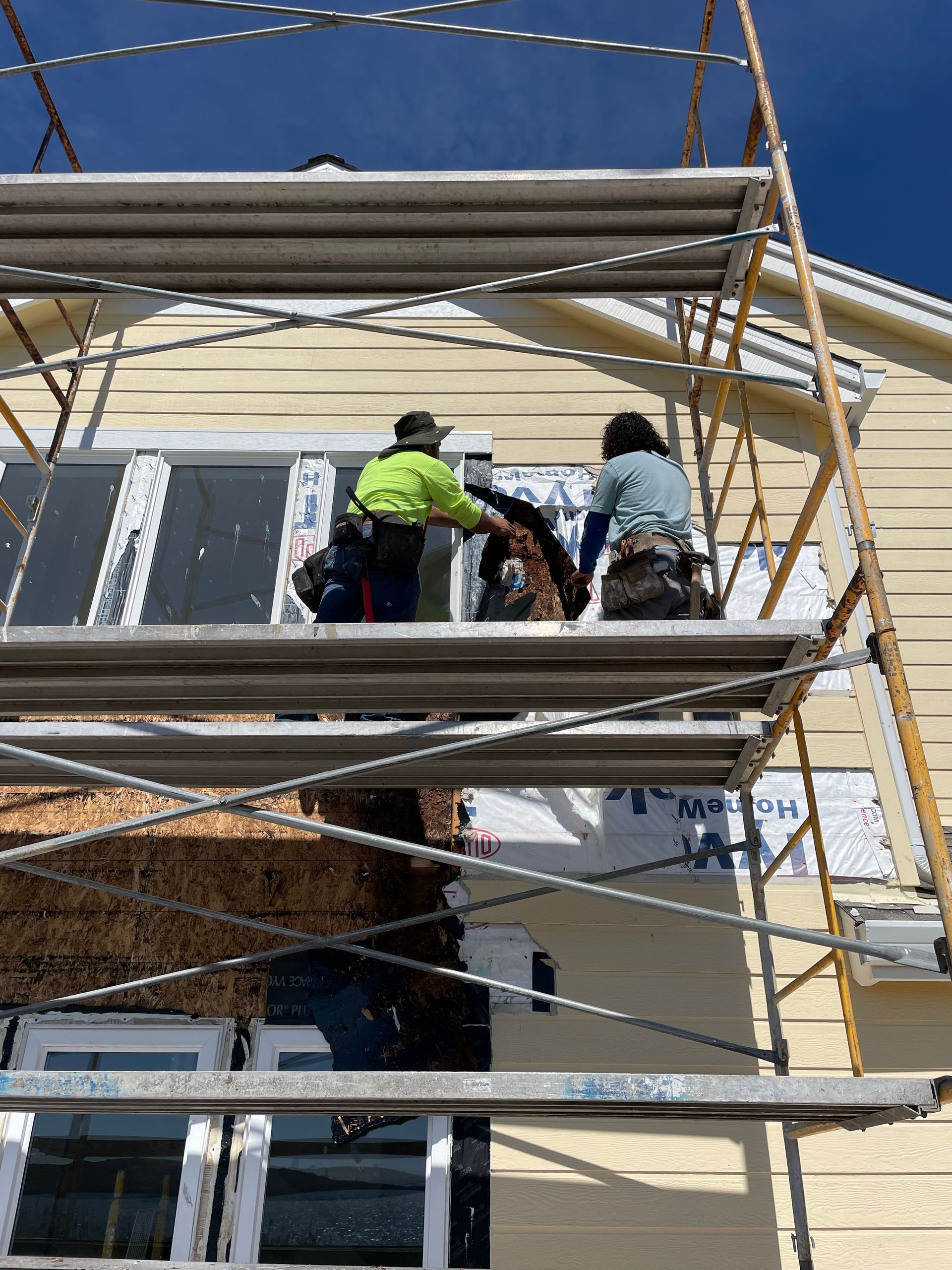 Workers on scaffolding painting a house exterior beneath a blue sky