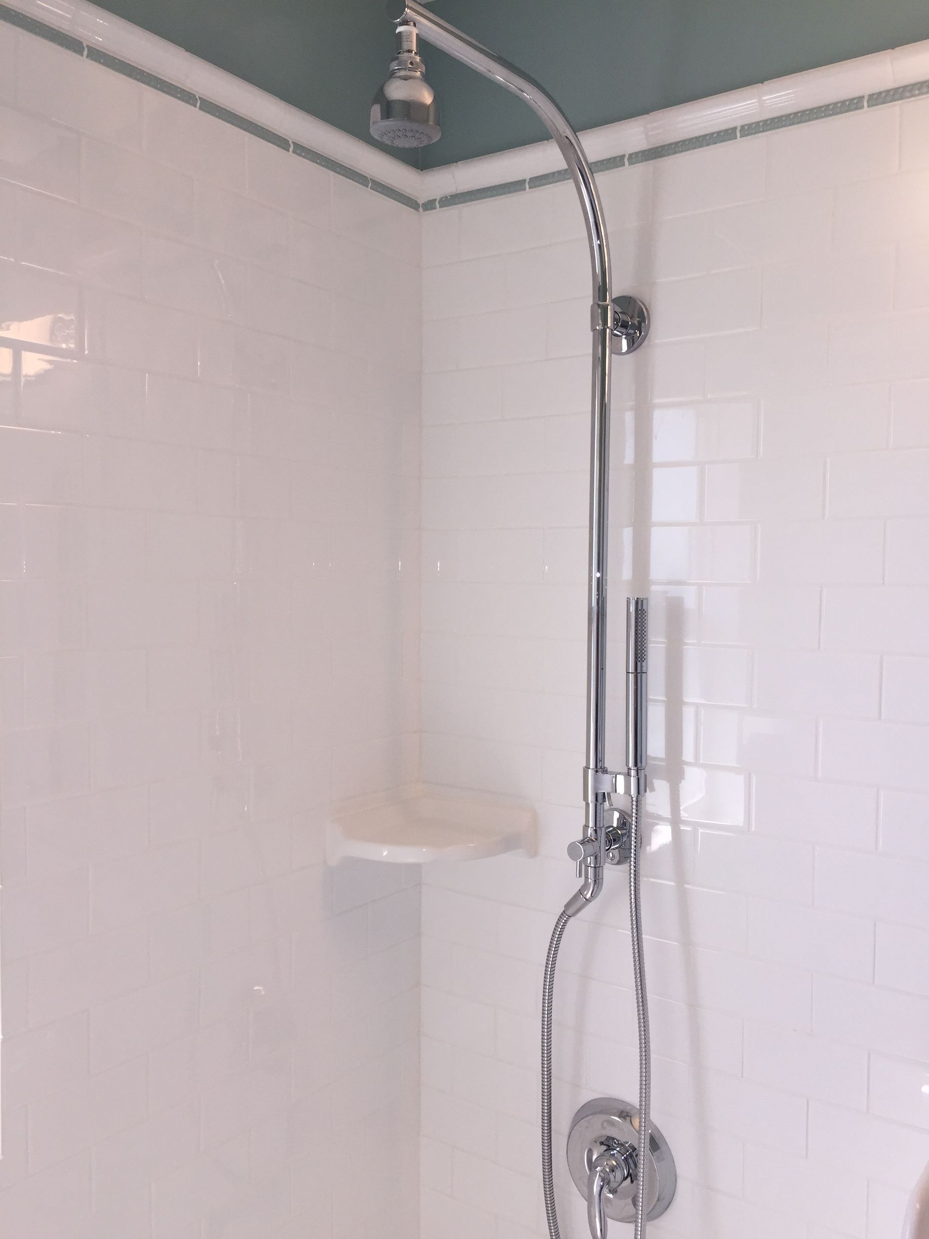 White tiled shower with chrome showerhead, grab bar, soap shelf, and handheld shower hose