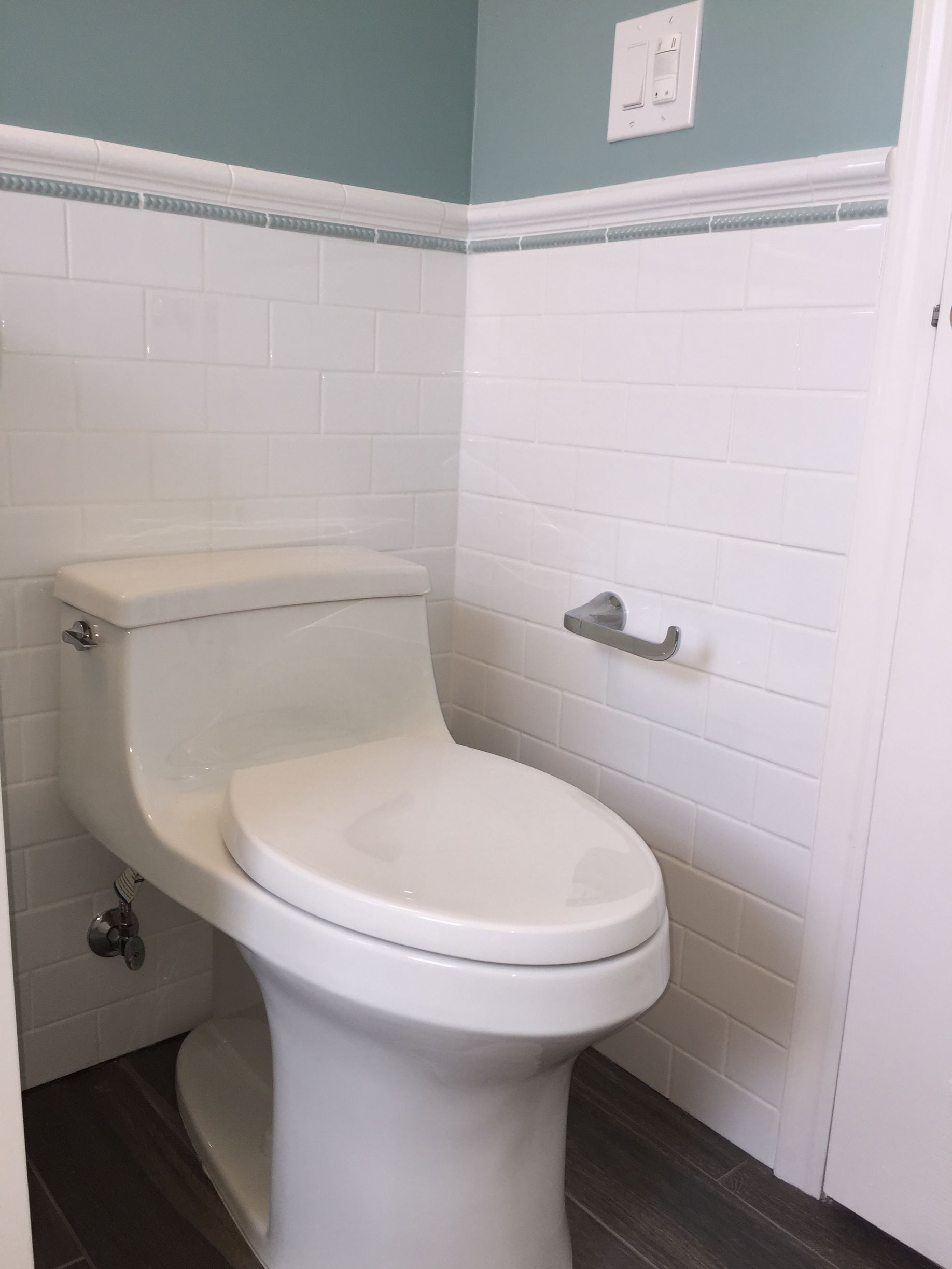 Accessible bathroom with a white toilet beside white tiled walls and a wall-mounted toilet paper holder.