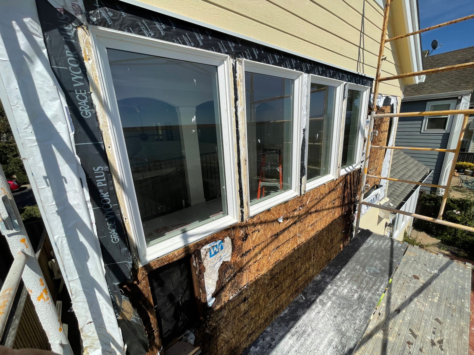 Exterior of a house with white-trim windows and siding under renovation, with scaffolding beside it