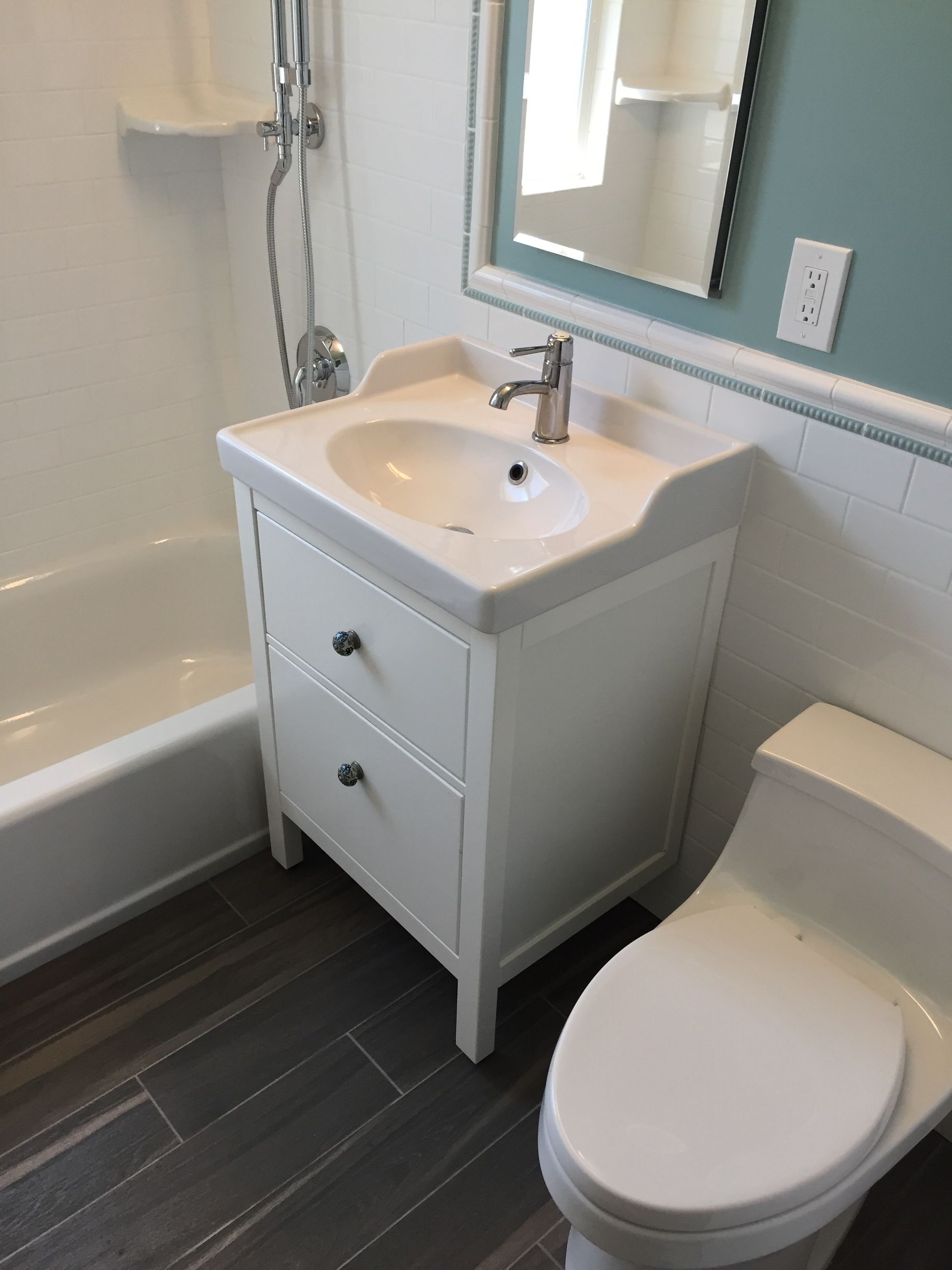 Small bathroom with white vanity, sink, toilet, mirror, and partial bathtub on dark tile floor.