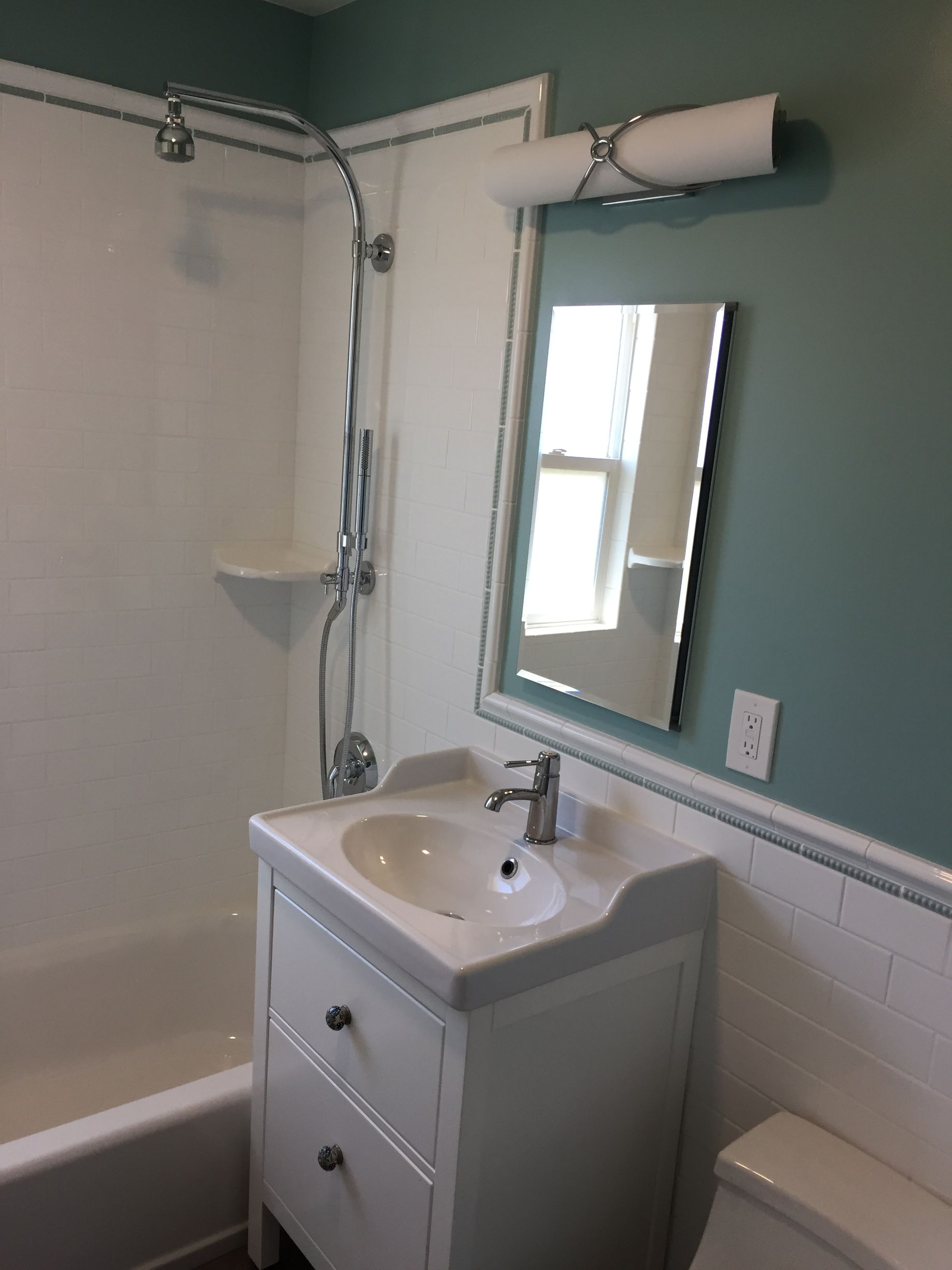 Bathroom with white vanity and sink, mirror, tub-shower, and a wall-mounted light fixture.
