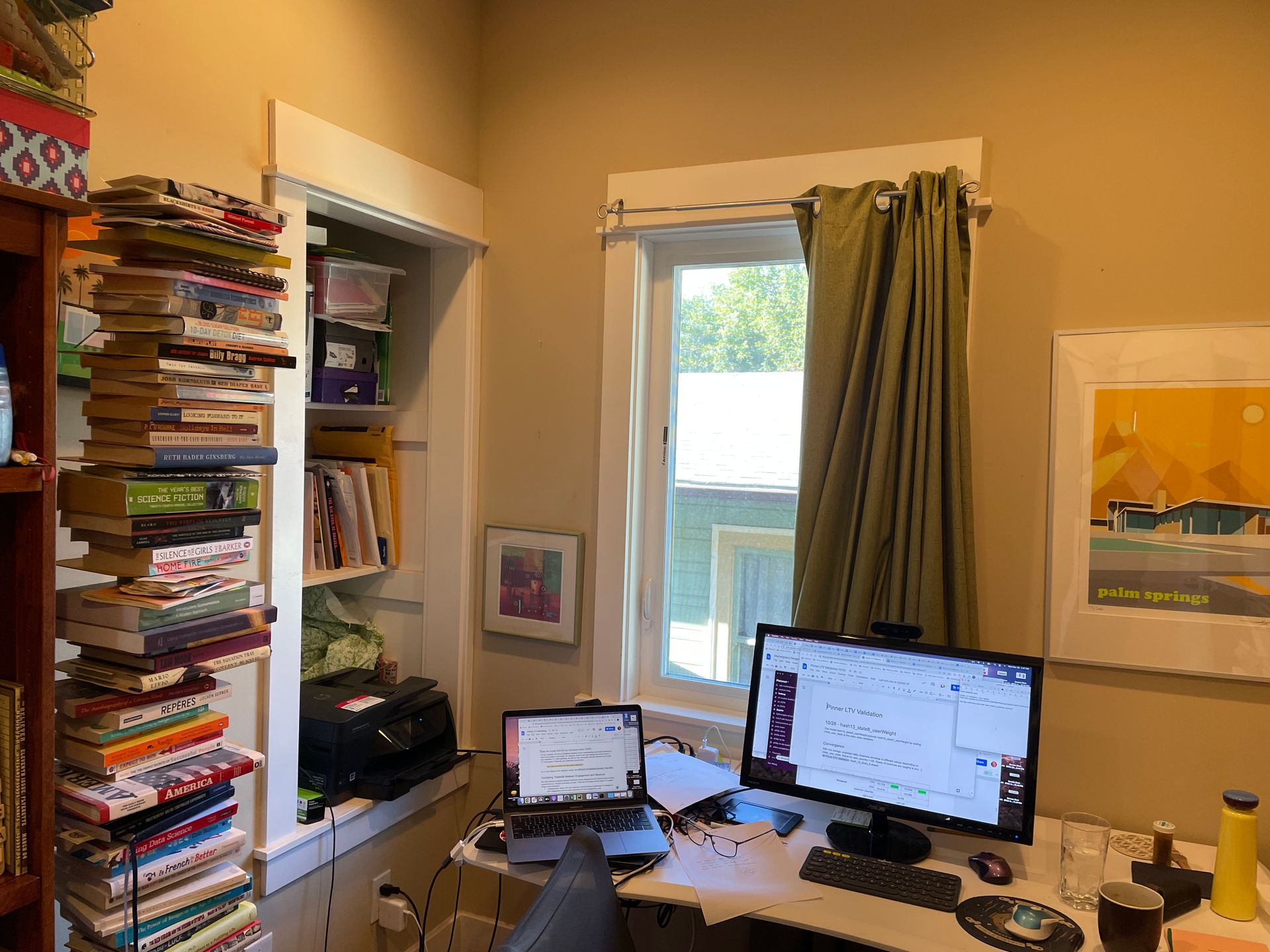 Home office with a desk, computer monitor, laptop, bookshelves, and a window with curtains.