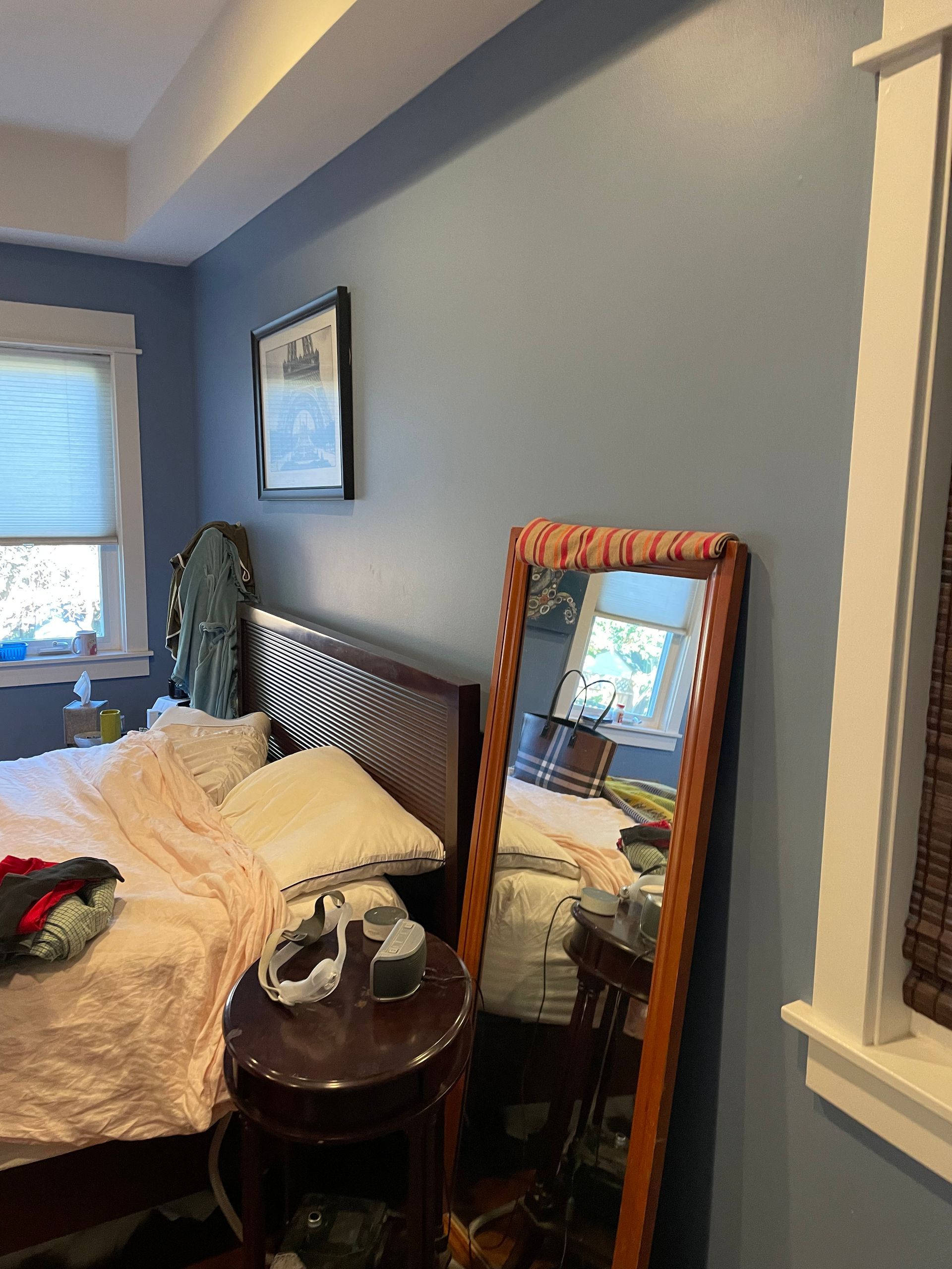 Bedroom with an unmade bed, leaning mirror, and window on blue-gray walls.