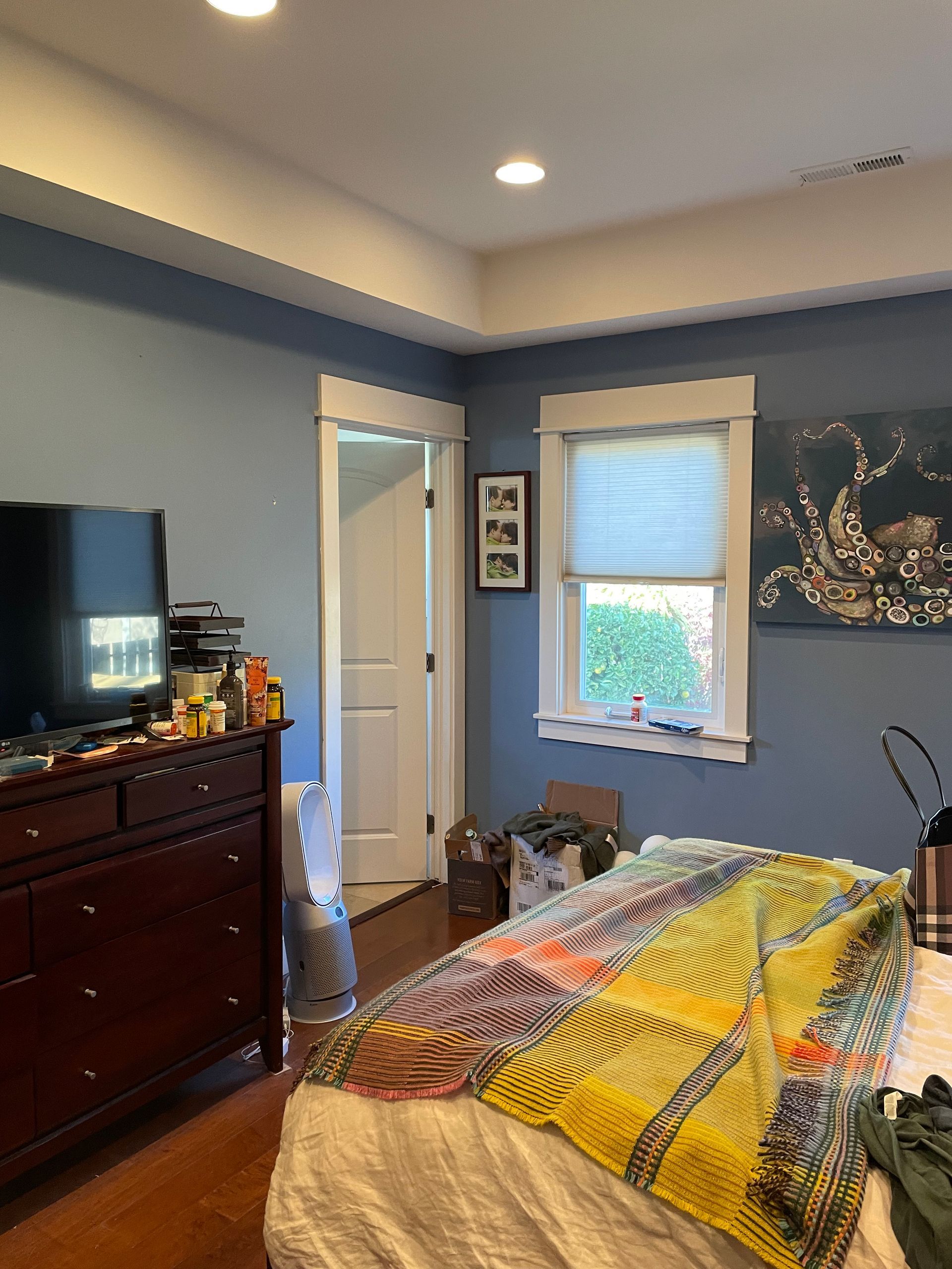 Bedroom with blue walls, dresser, window, bed with yellow plaid blanket, and wall art.