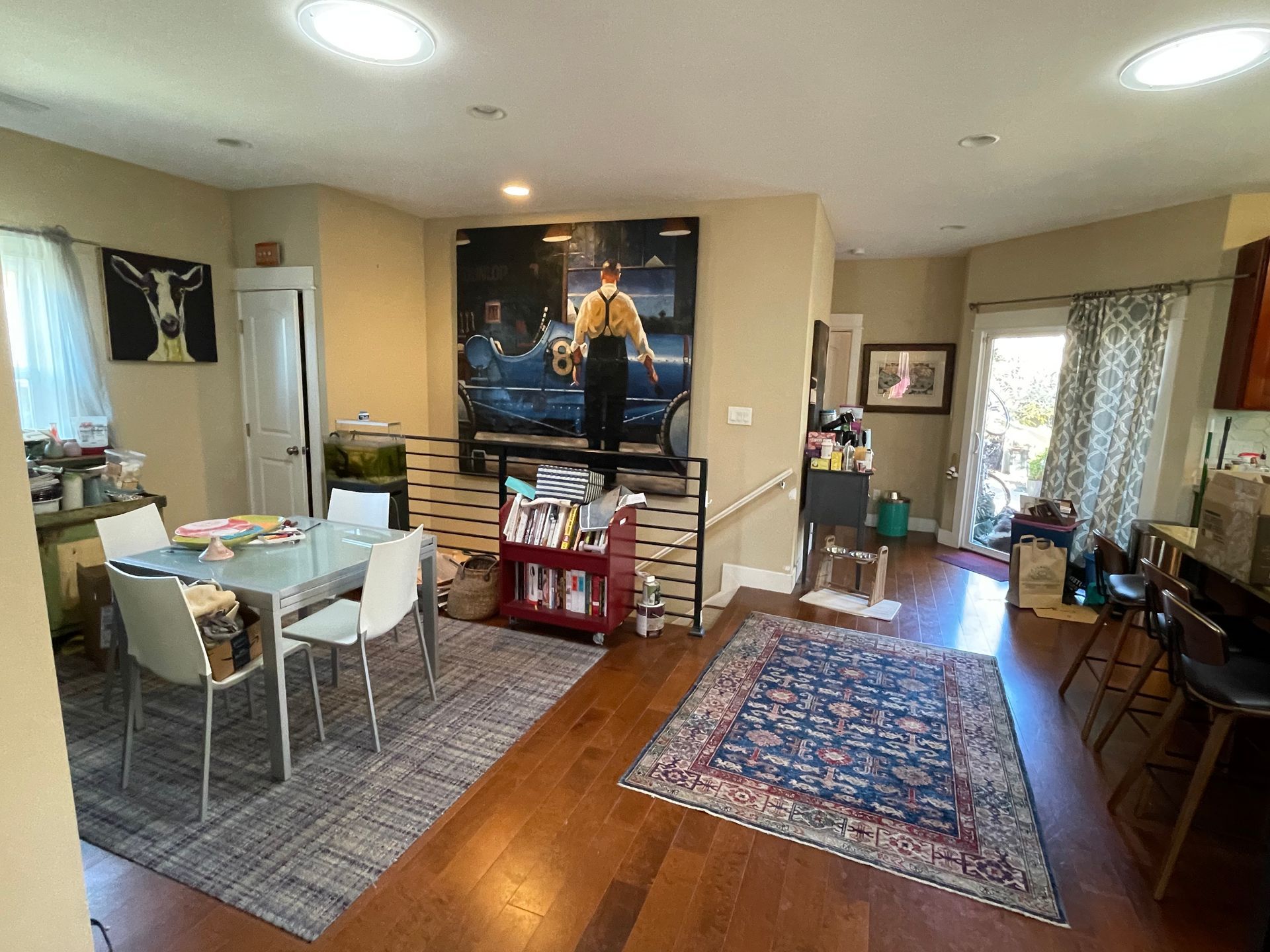 Open-plan living and dining room with hardwood floors, rugs, table, chairs, and large wall art.