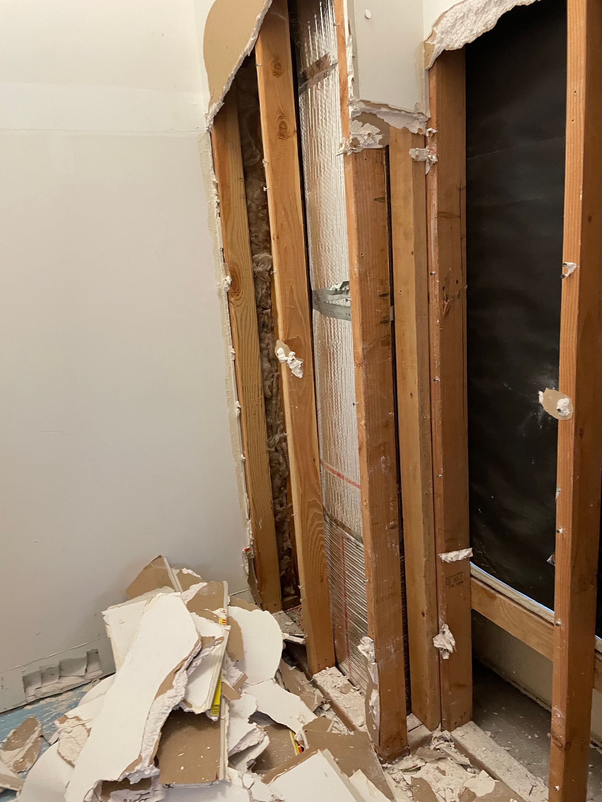 Damaged interior wall with exposed studs, insulation, and debris on the floor.