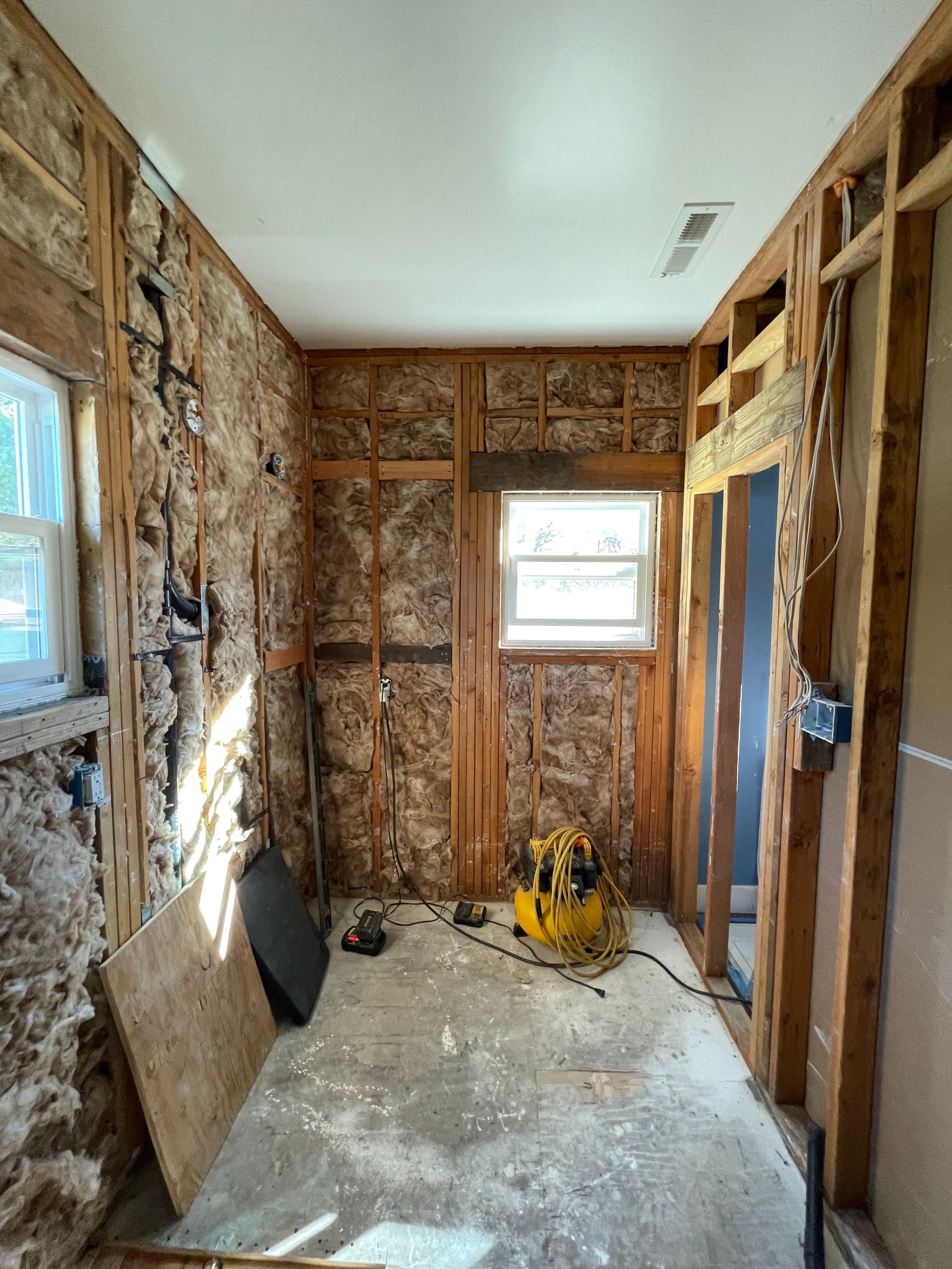 Narrow unfinished room with exposed studs, insulation, windows, and a yellow tool on the floor